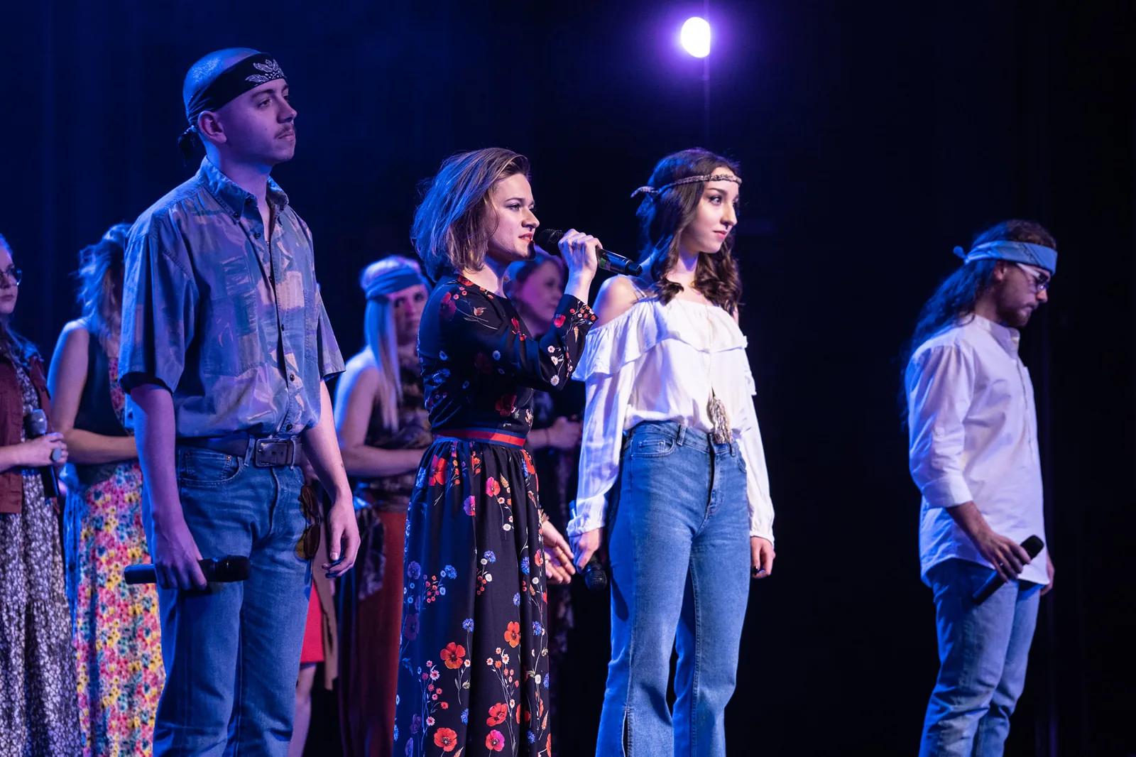 Grupa wokalistów wykonuje utwór w szeregu na scenie.