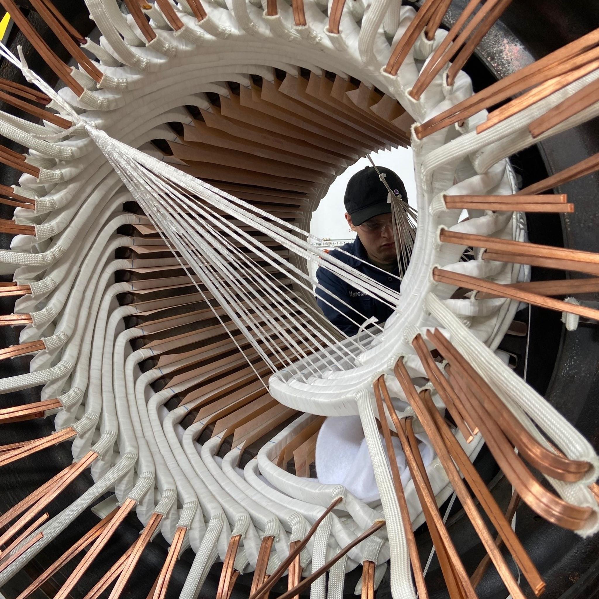 Technician installs insulated copper windings in a large electric motor stator.