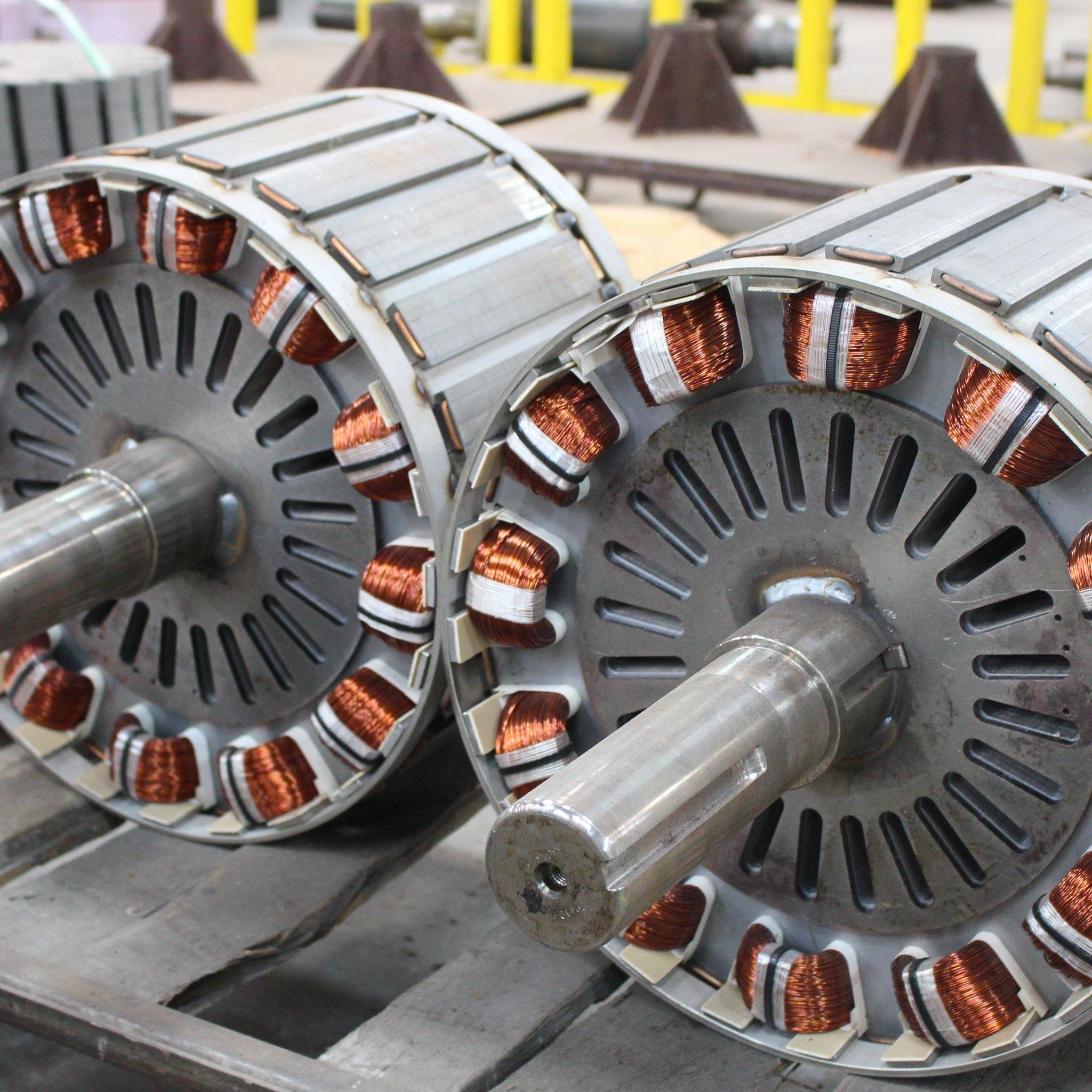 Two large electric motor rotors with copper windings and steel shafts sit on a workshop table.