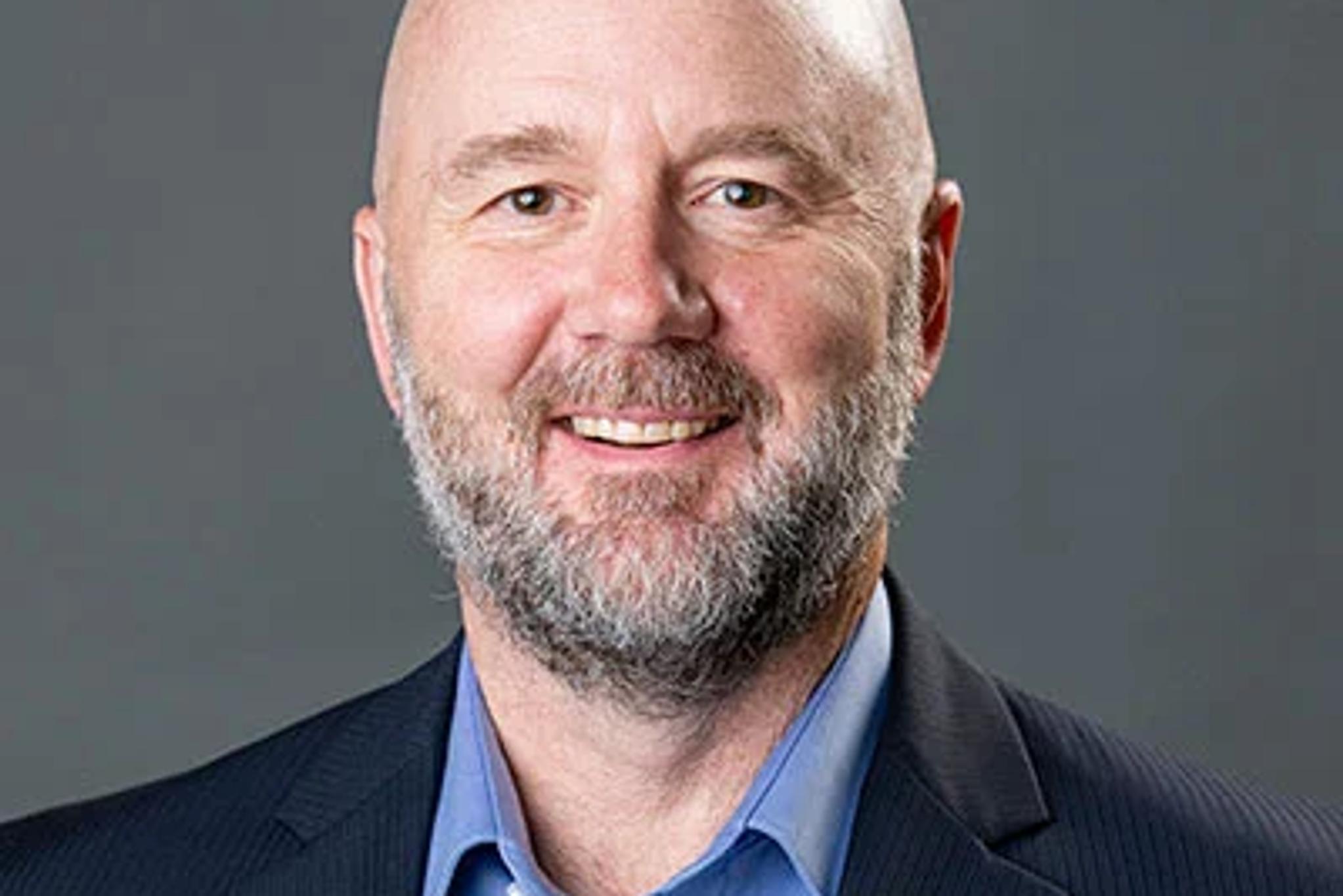 Headshot of a smiling bald man with a gray beard wearing a blue shirt and dark blazer.