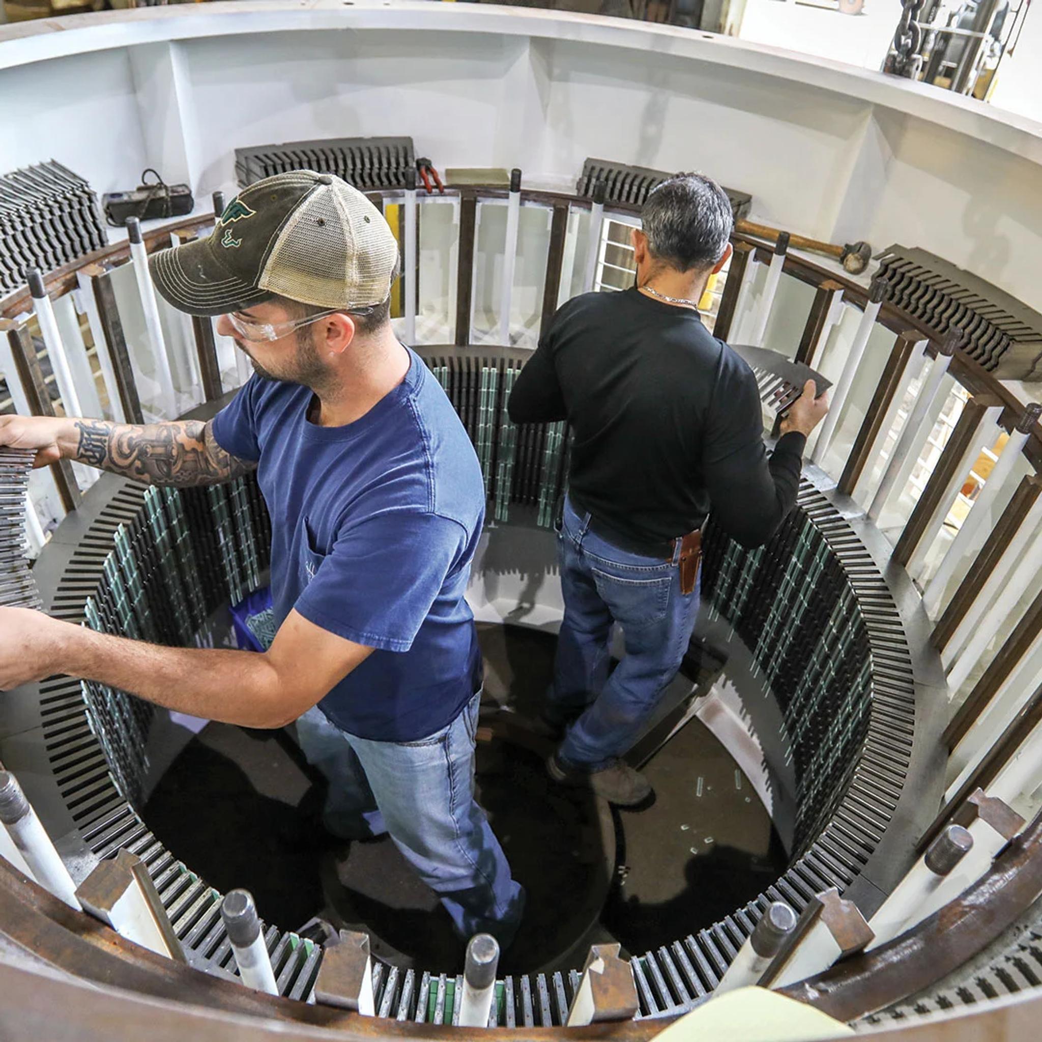 Technicians install stator core laminations inside a large electric generator.