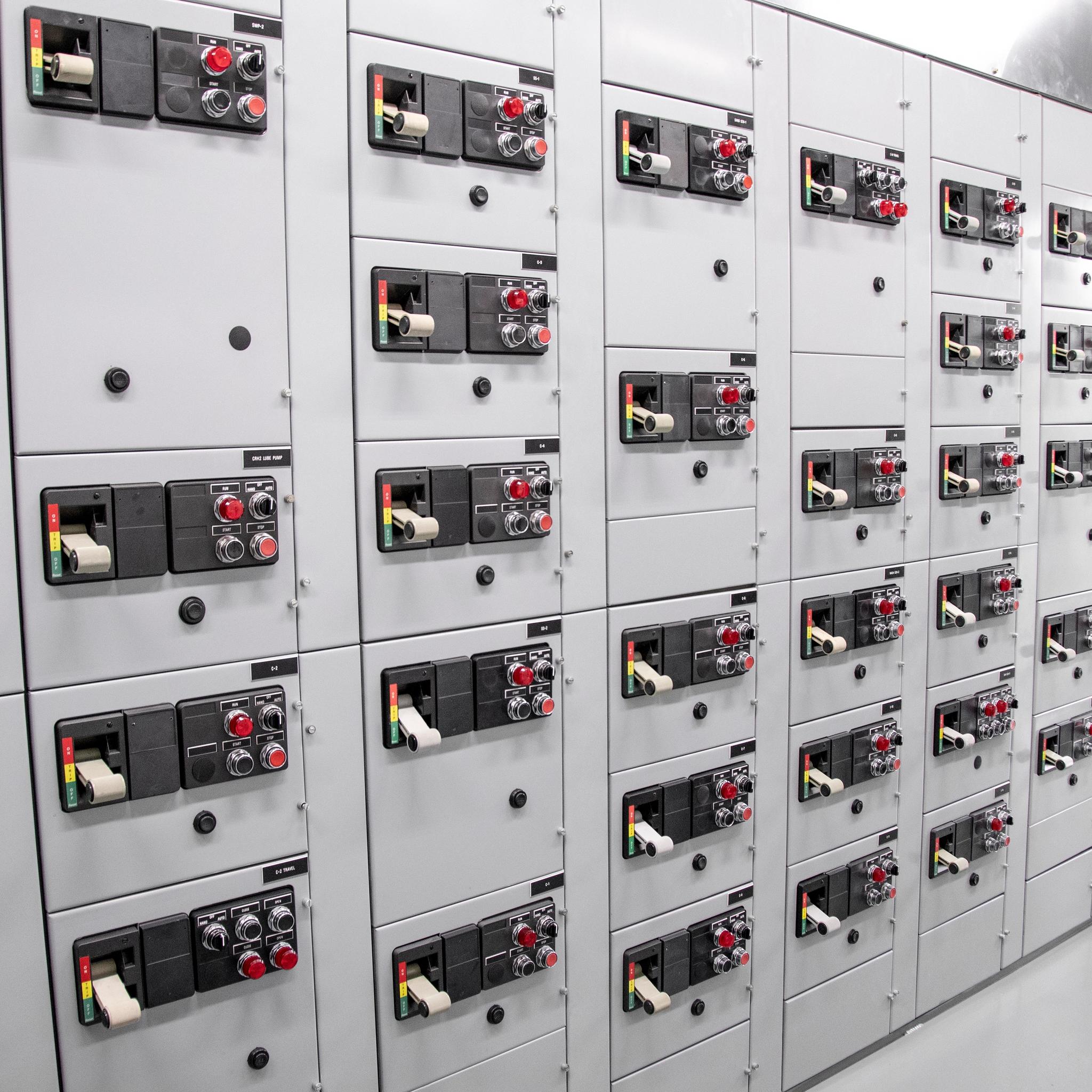 Rows of electrical switchgear cabinets with circuit breakers, control switches, and indicator lights.