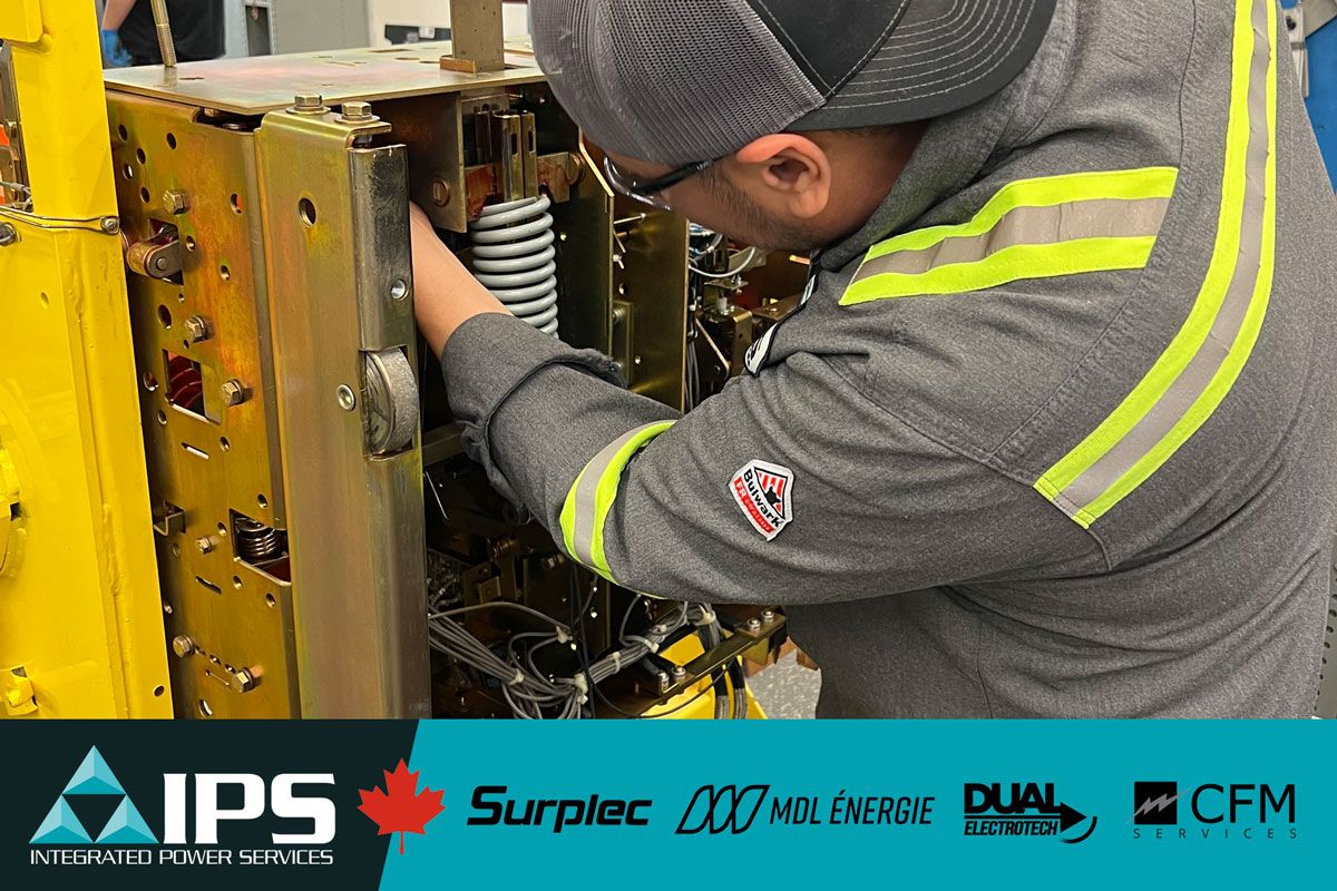 A technician in a grey uniform with reflective stripes and a cap works on complex industrial equipment.