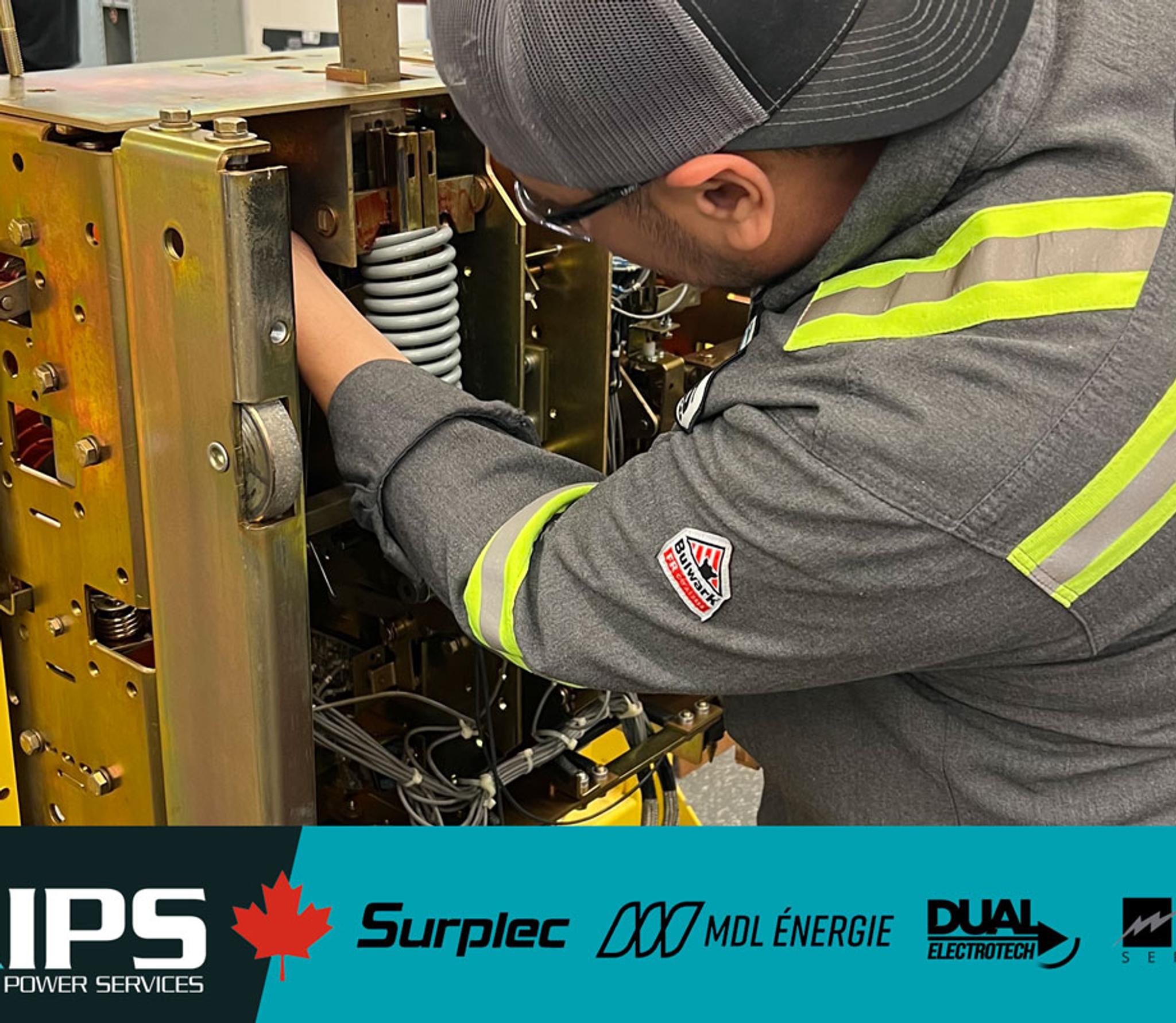 A technician in a grey uniform with reflective stripes and a cap works on complex industrial equipment.
