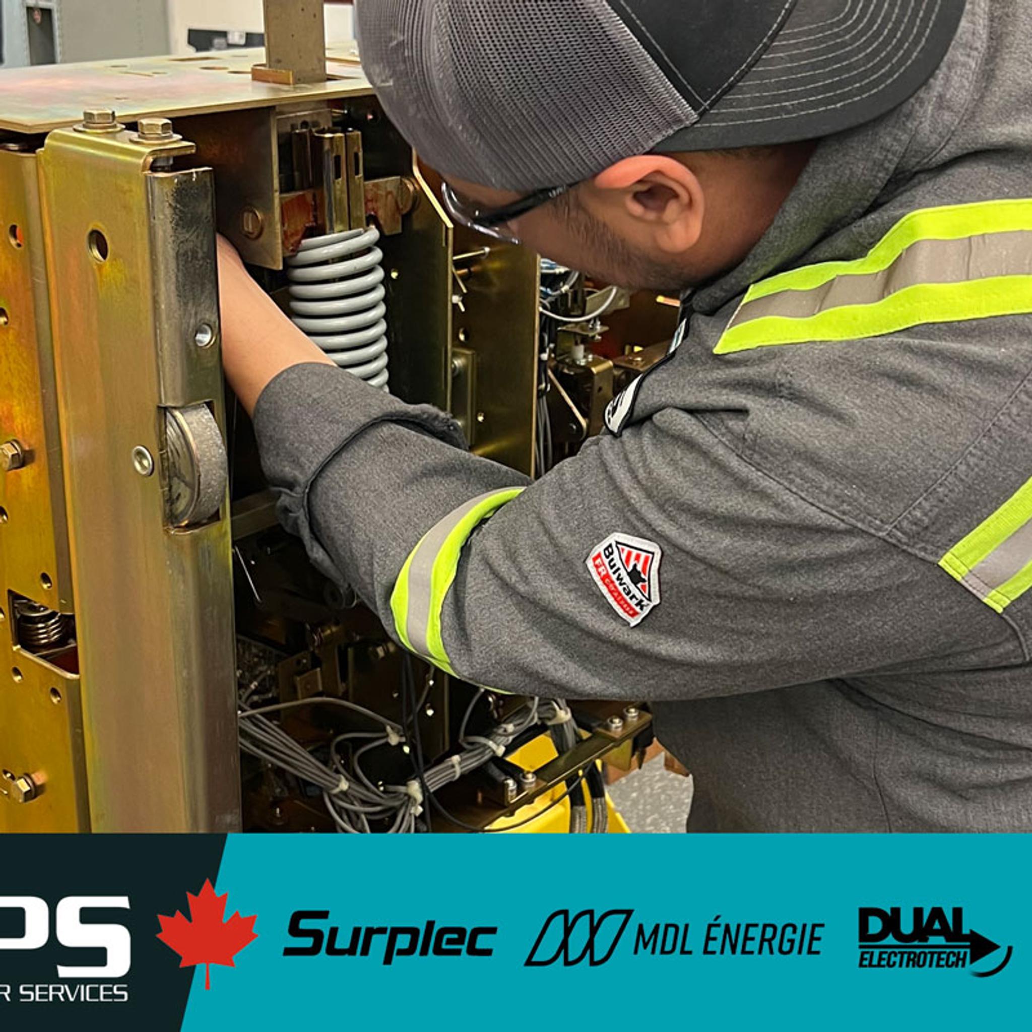 A technician in a grey uniform with reflective stripes and a cap works on complex industrial equipment.