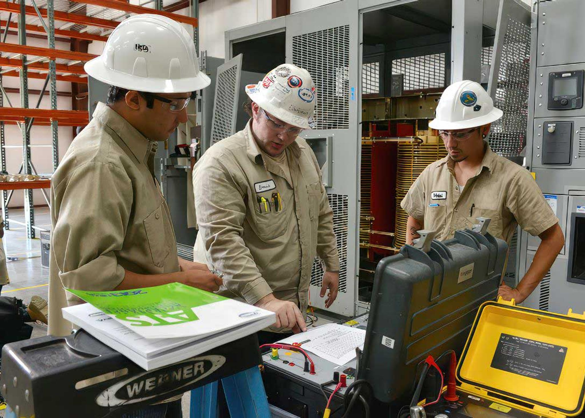 Three technicians inspect electrical test equipment beside an open industrial transformer enclosure.