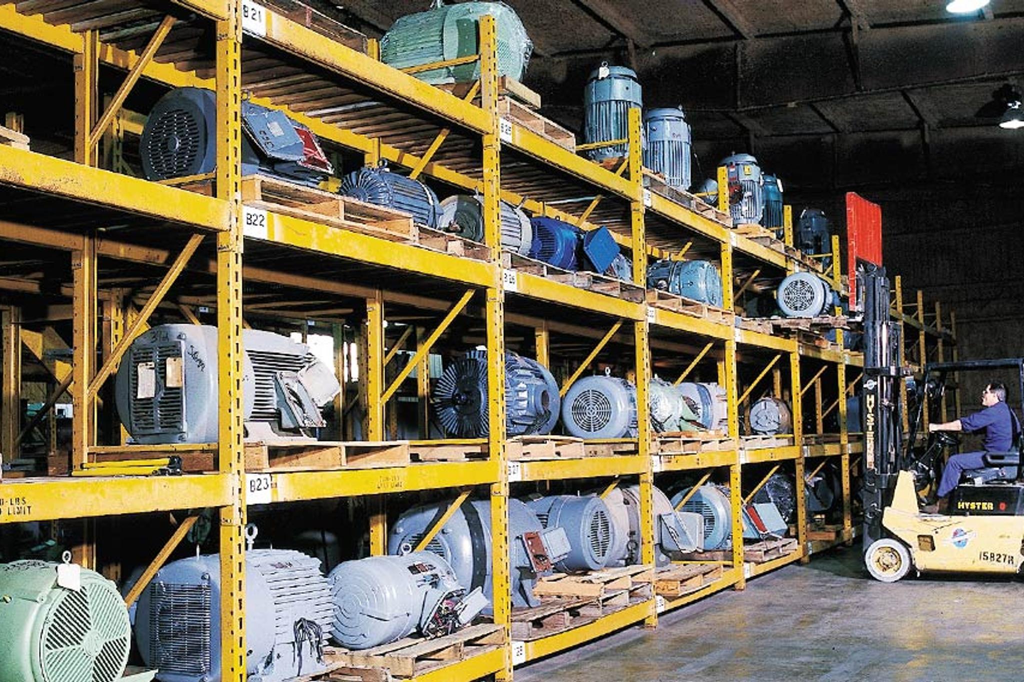Worker operates a forklift beside warehouse racks filled with industrial electric motors.