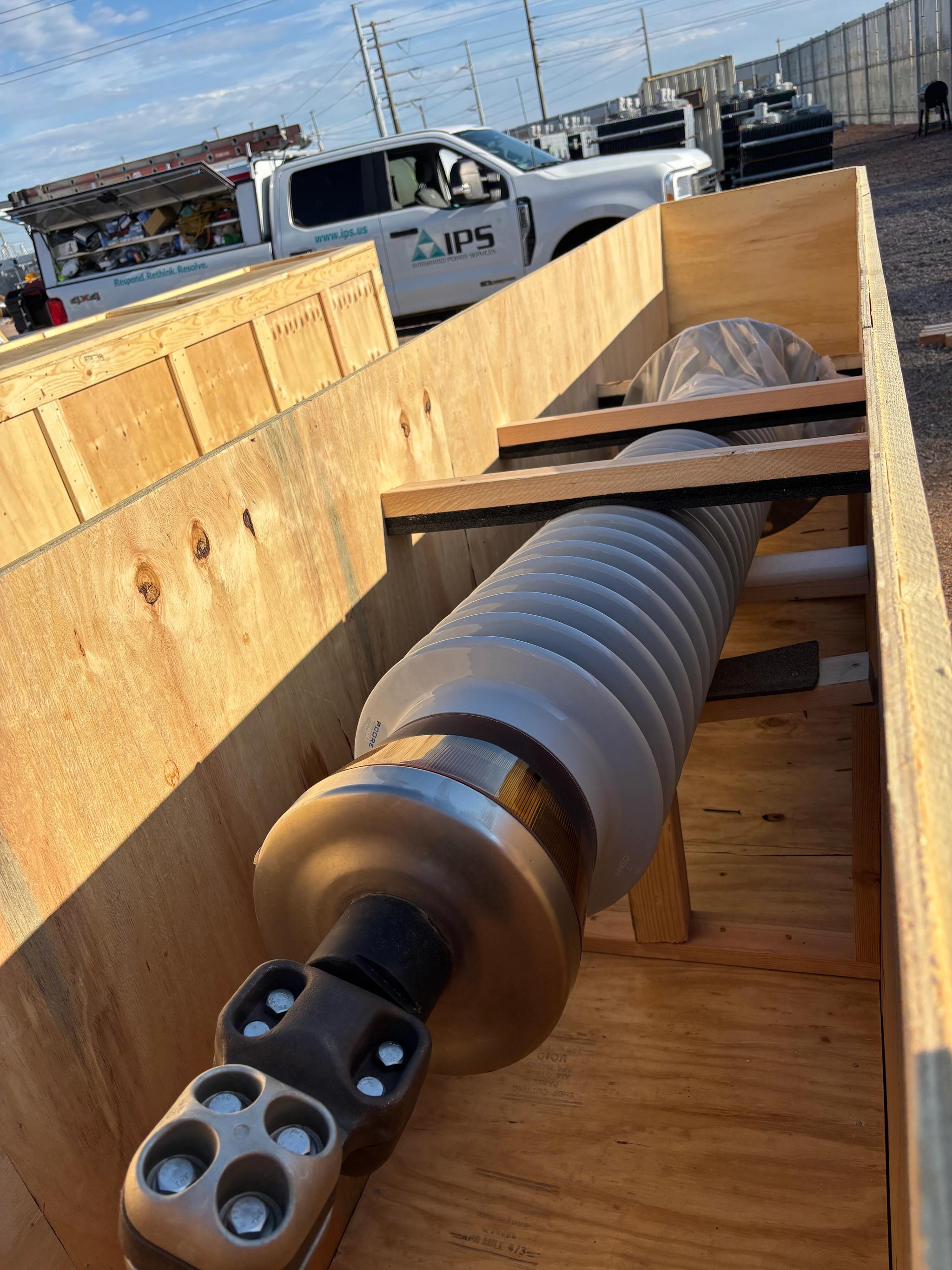 High-voltage electrical bushing secured in a wooden shipping crate beside an IPS service truck.