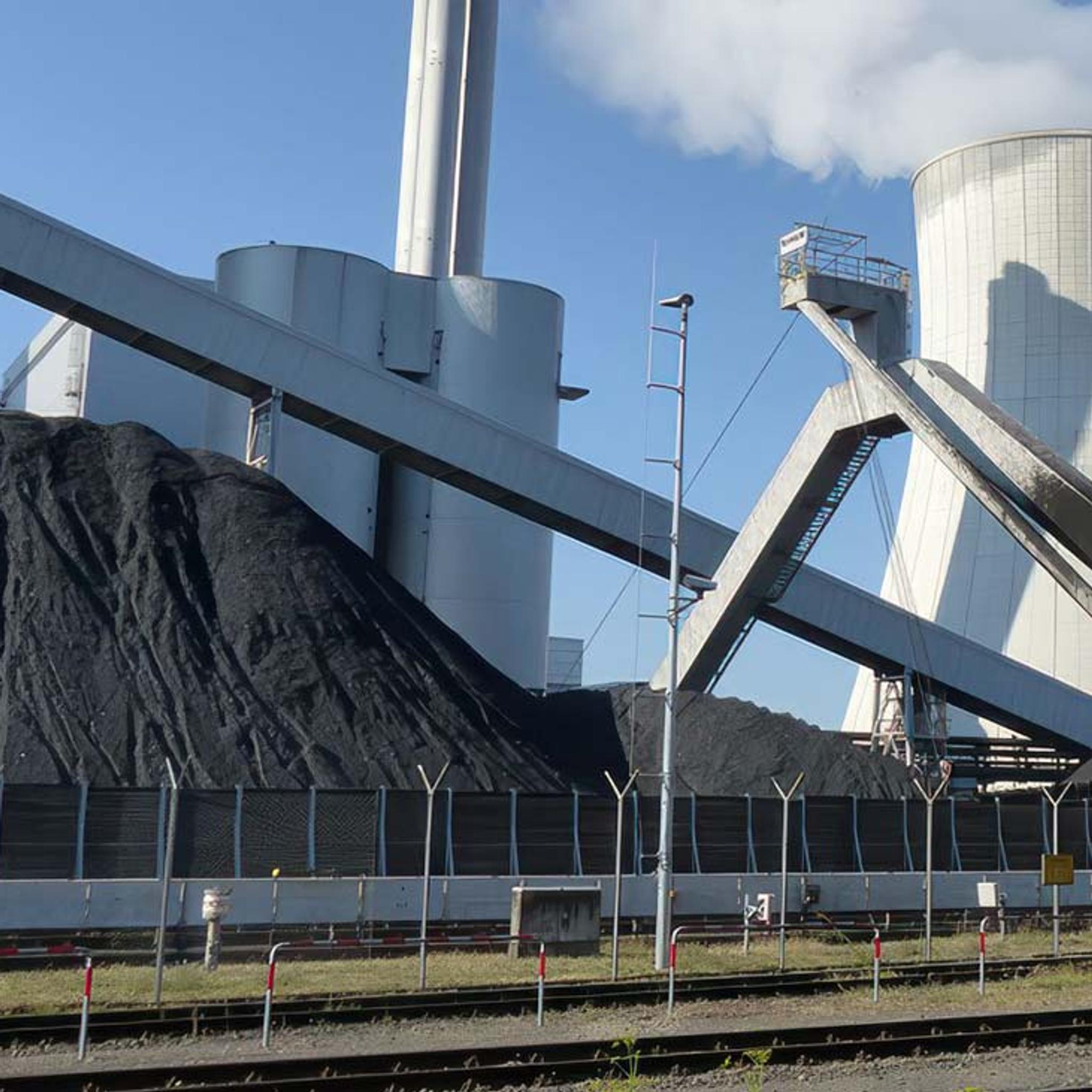 Coal-fired power plant with coal piles, conveyor belts, smokestacks and a cooling tower emitting steam.