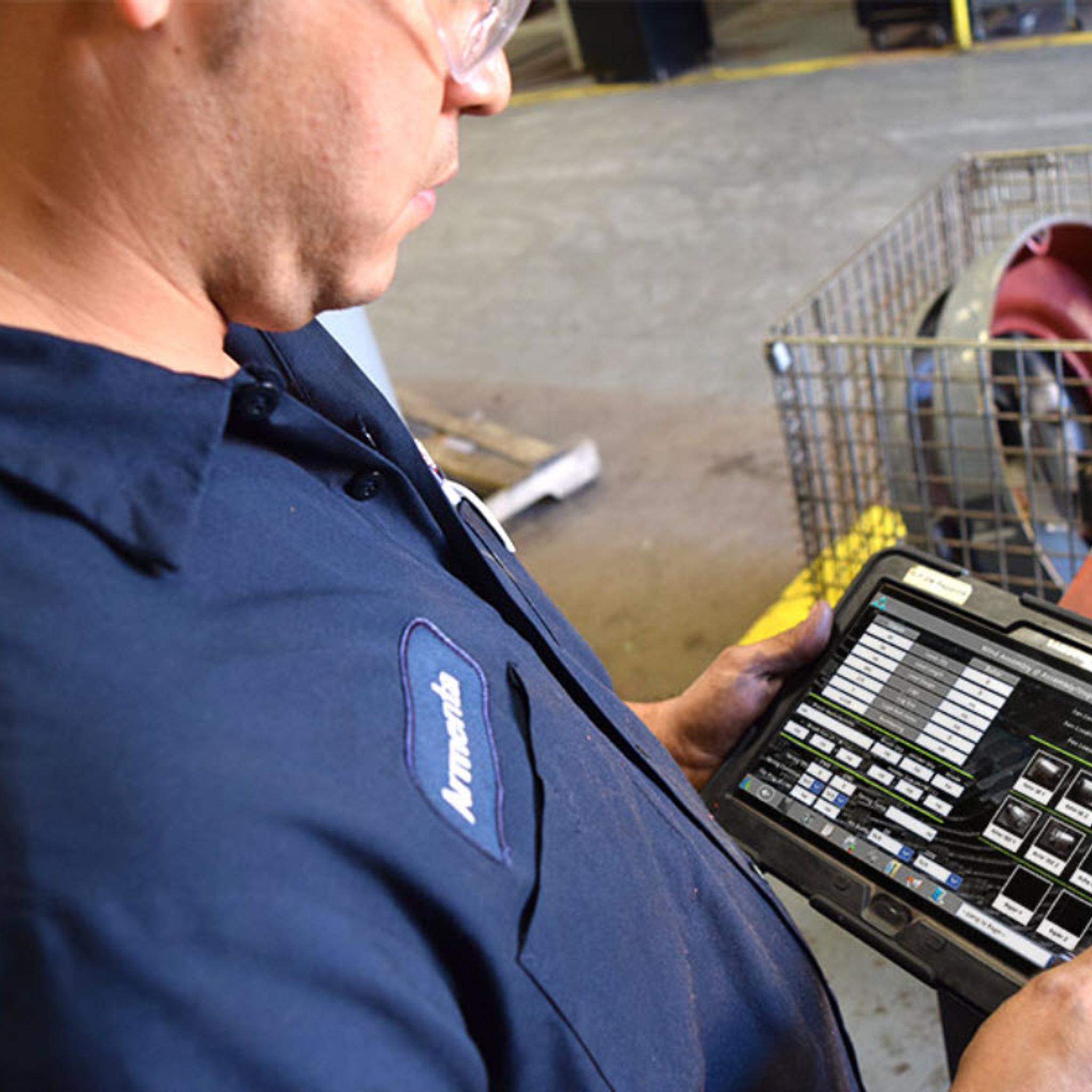 Technician uses a tablet to review equipment data beside an industrial motor.