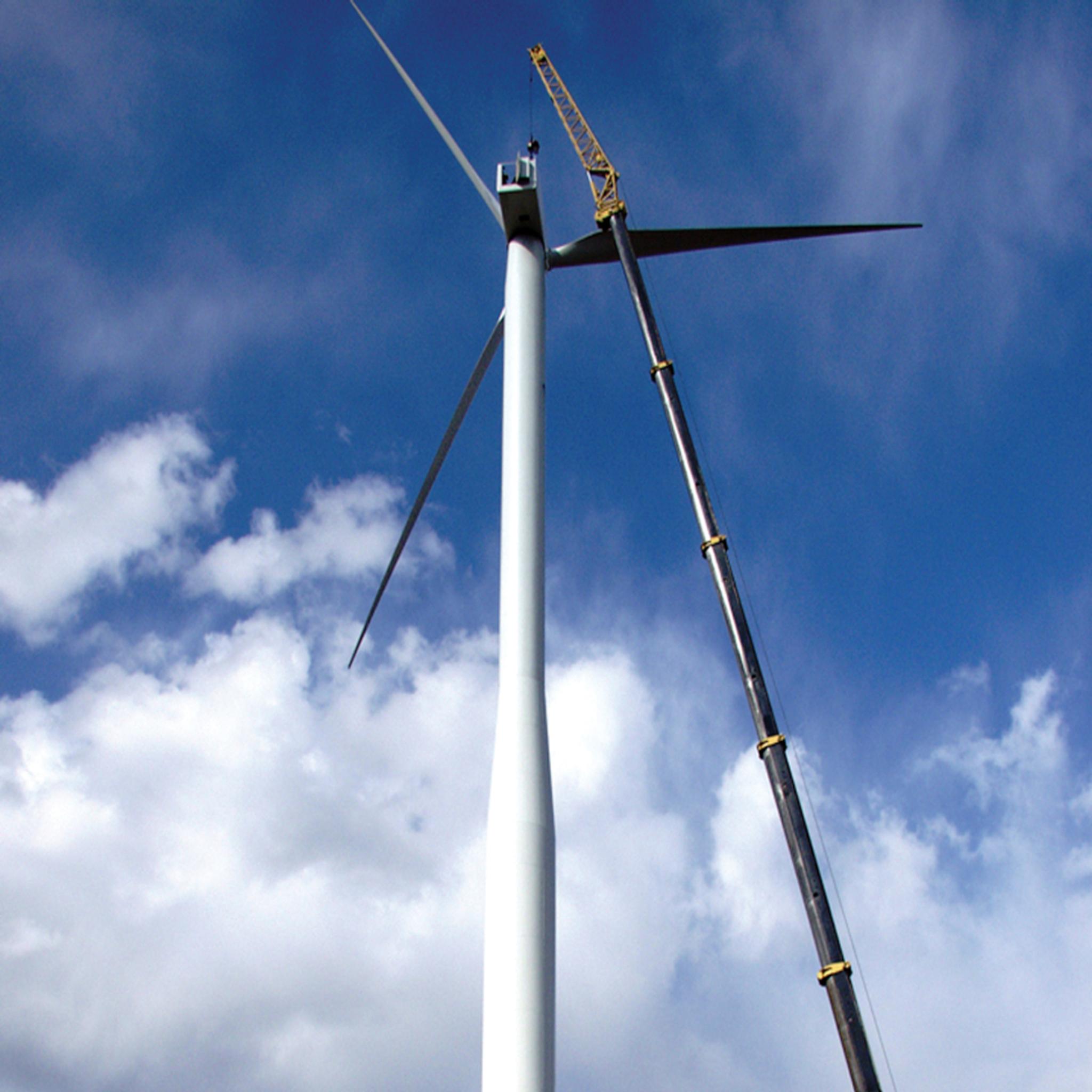 Crane installs a rotor blade on a wind turbine against a blue sky.