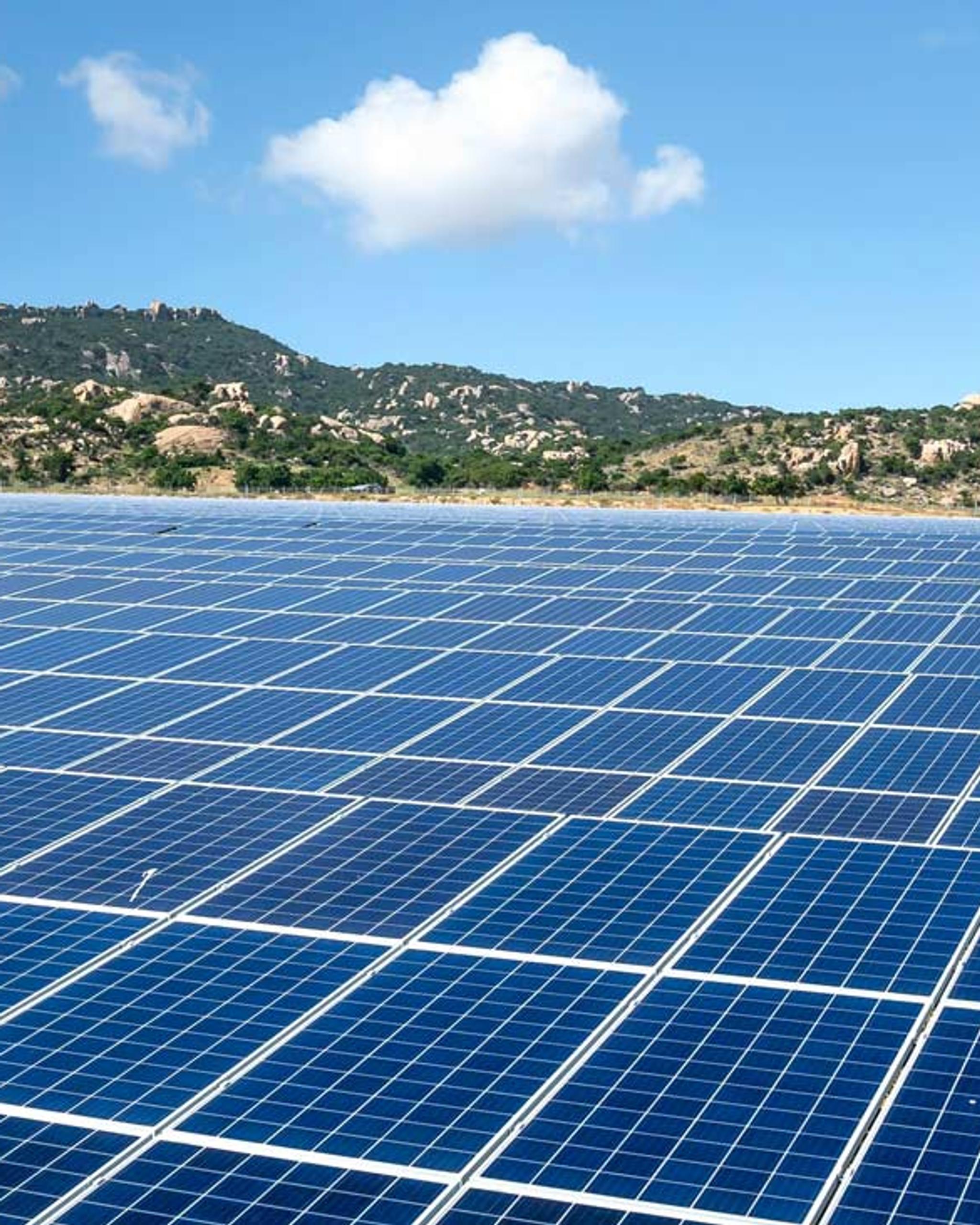 Vaste champ de panneaux solaires devant des collines rocheuses sous un ciel bleu.