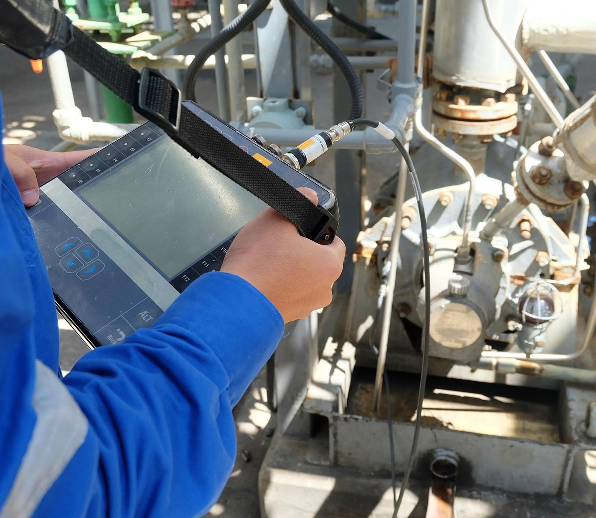 Un technicien contrôle une pompe industrielle à l’aide d’une tablette de diagnostic reliée par câble.