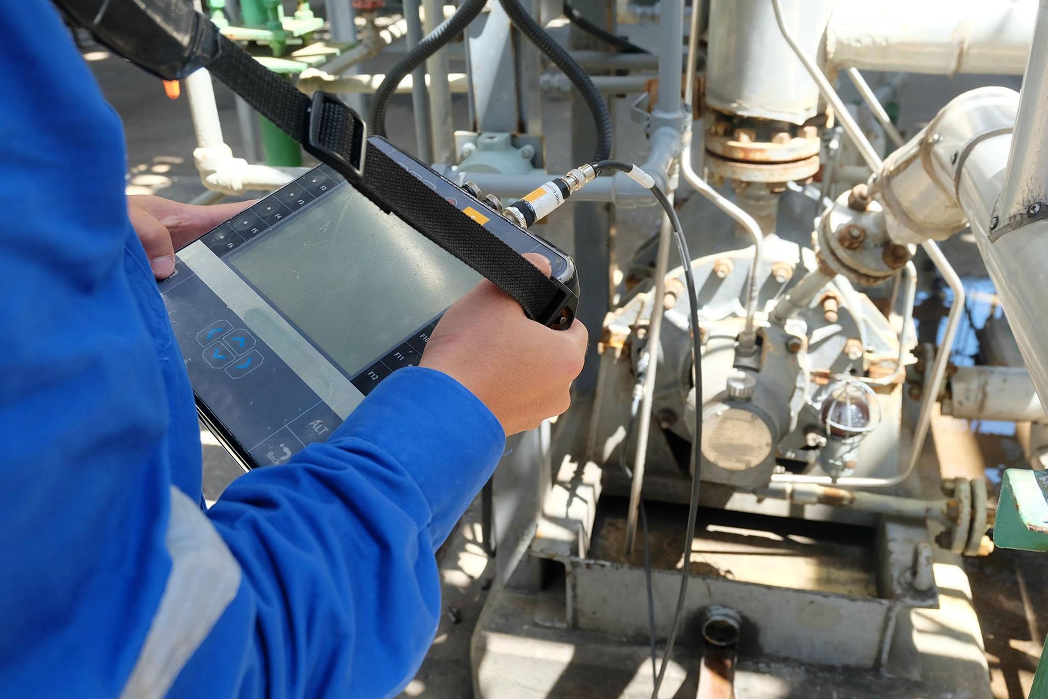 Technician uses a handheld vibration analyzer to inspect industrial pump equipment.