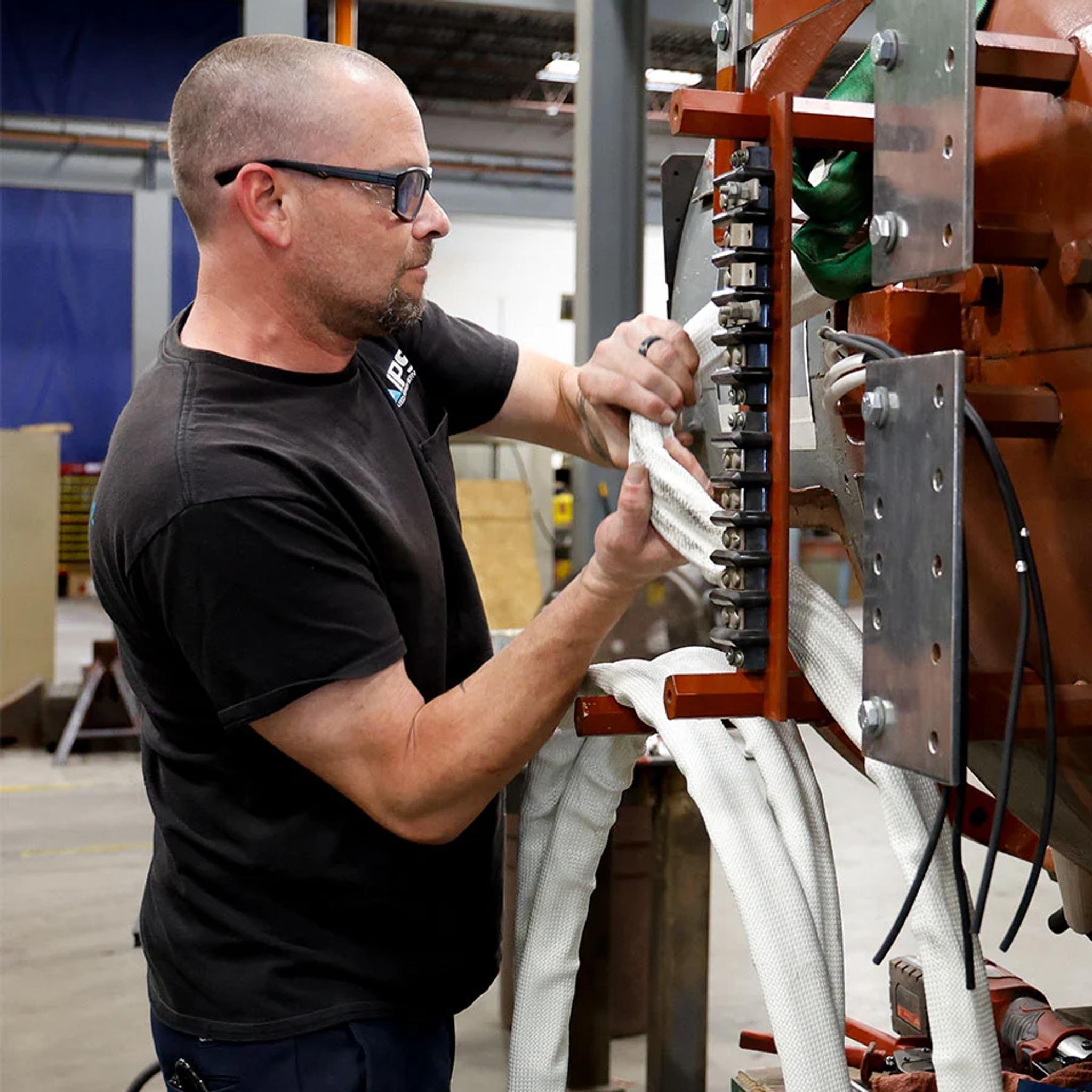 Technician installs insulated power cables on a large industrial transformer.