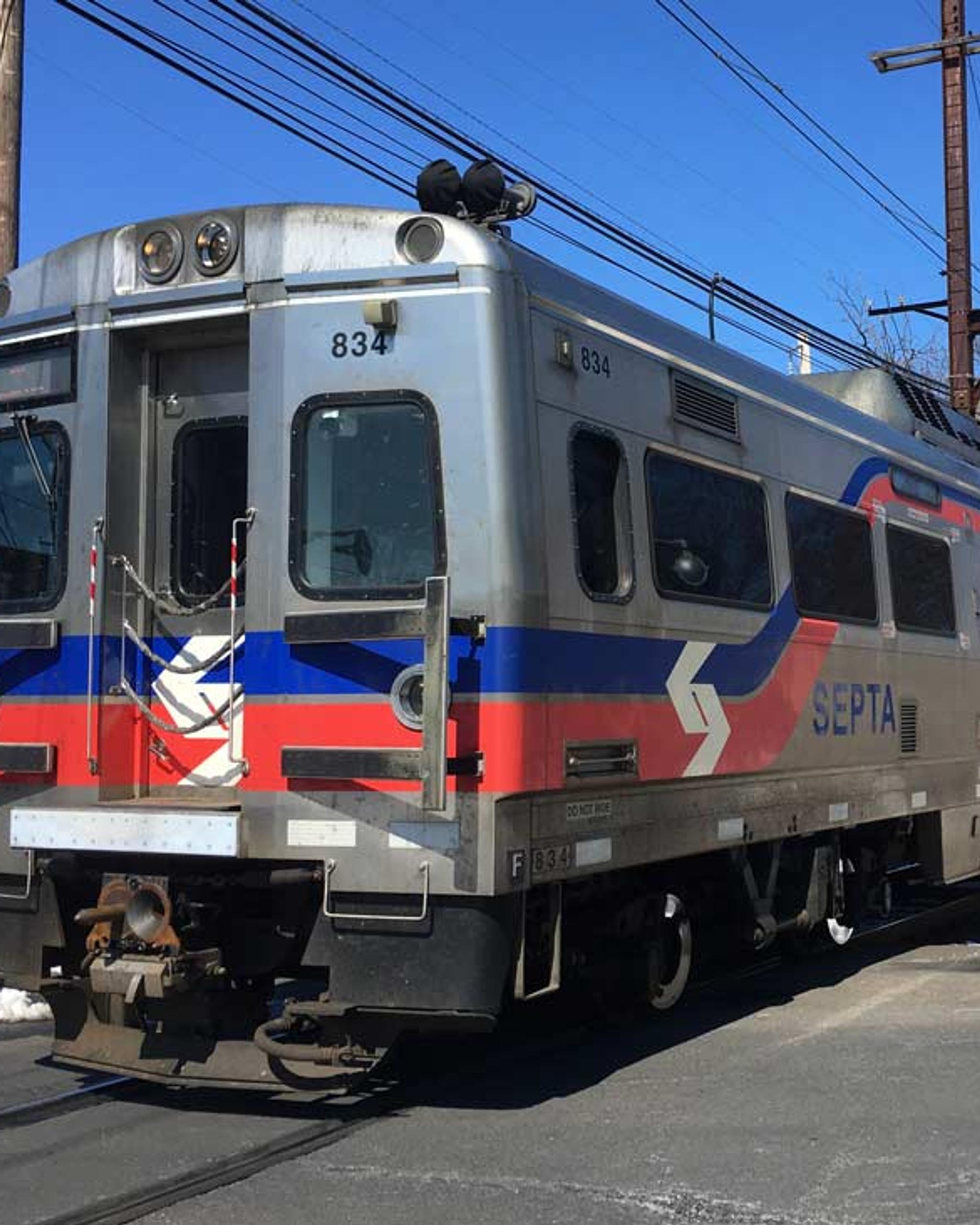 SEPTA electric commuter train crosses a snowy road beneath overhead power lines.