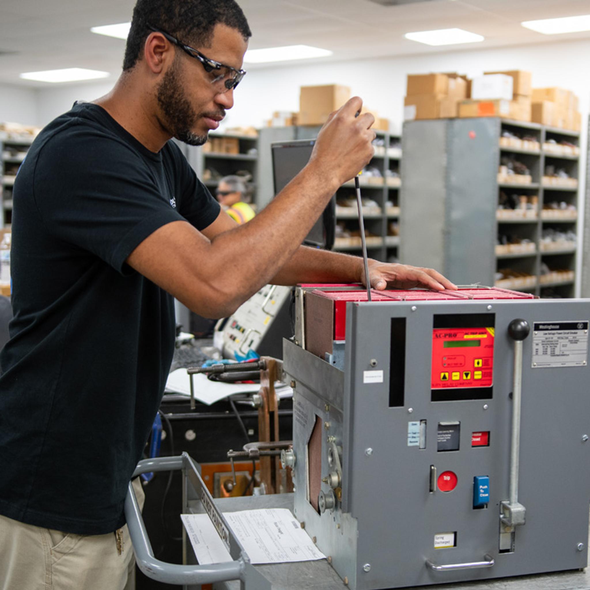 Technician uses a screwdriver to service an industrial circuit breaker in an electrical repair shop.