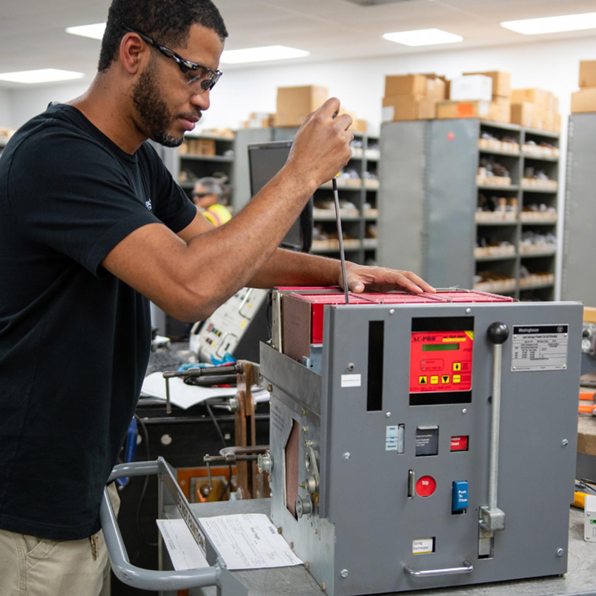 Technician uses a screwdriver to service an industrial circuit breaker in an electrical repair shop.