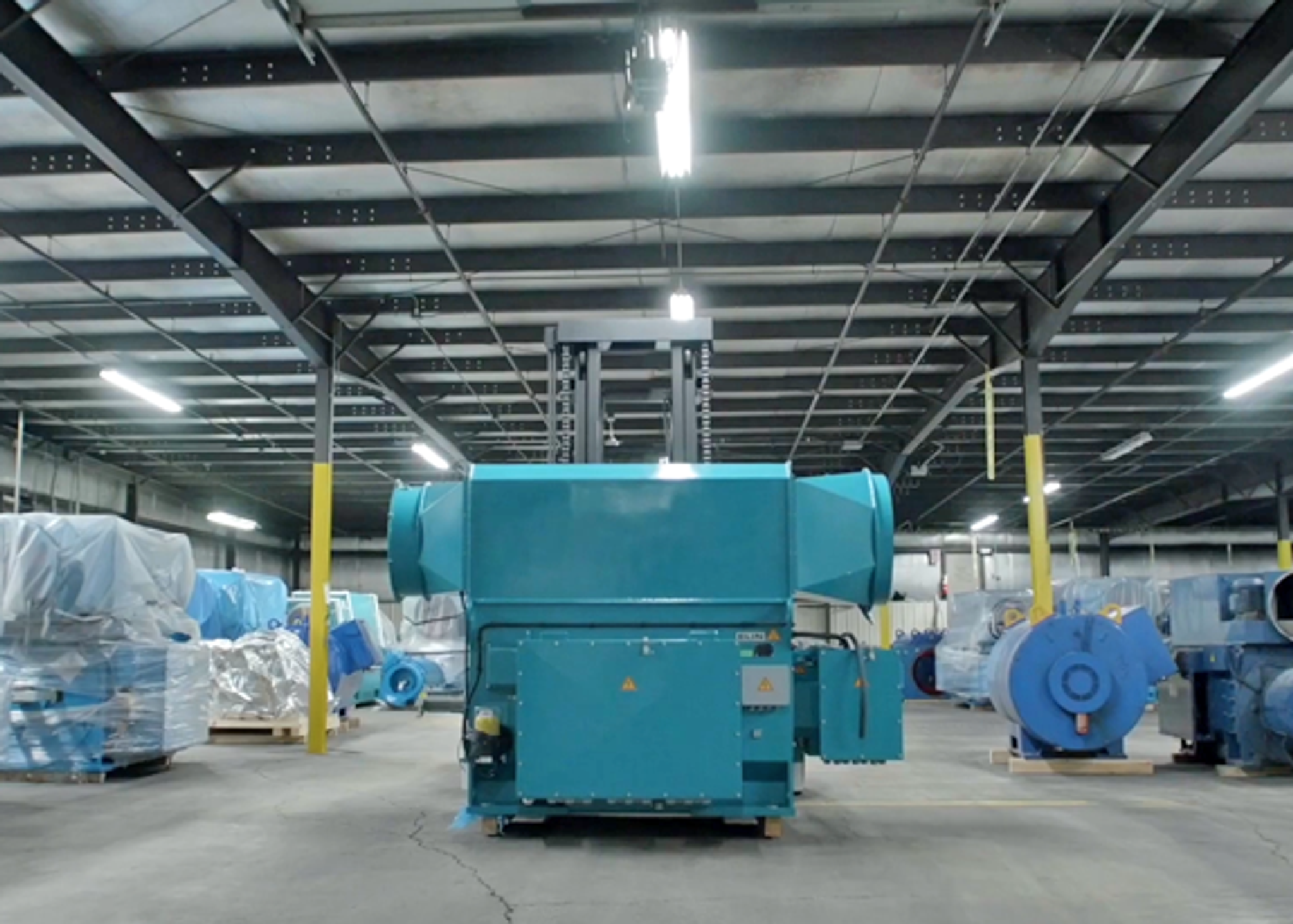 Large industrial electric motor on a factory floor surrounded by covered and stored equipment.