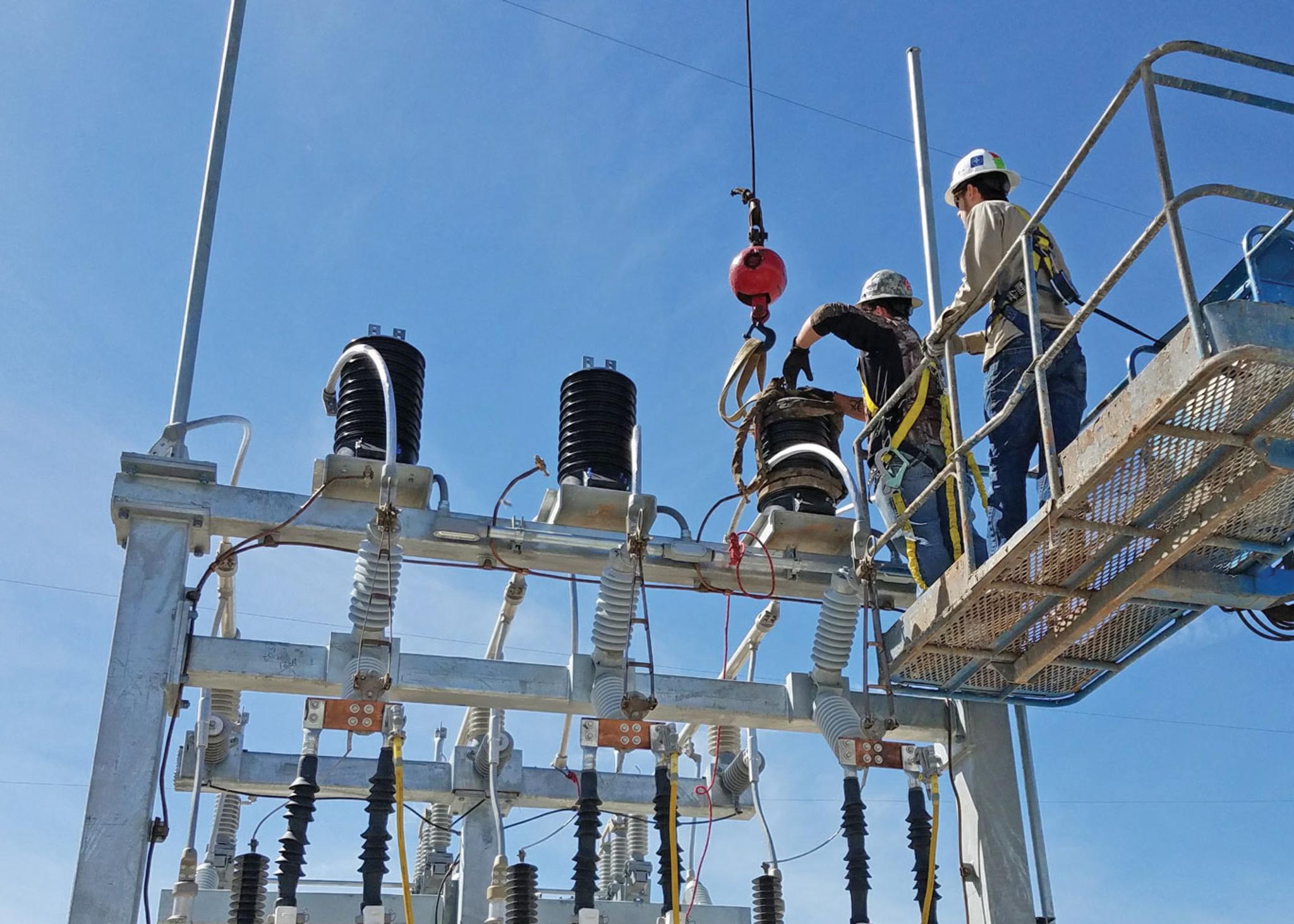 Technicians use a boom lift and crane to service high-voltage substation switchgear.