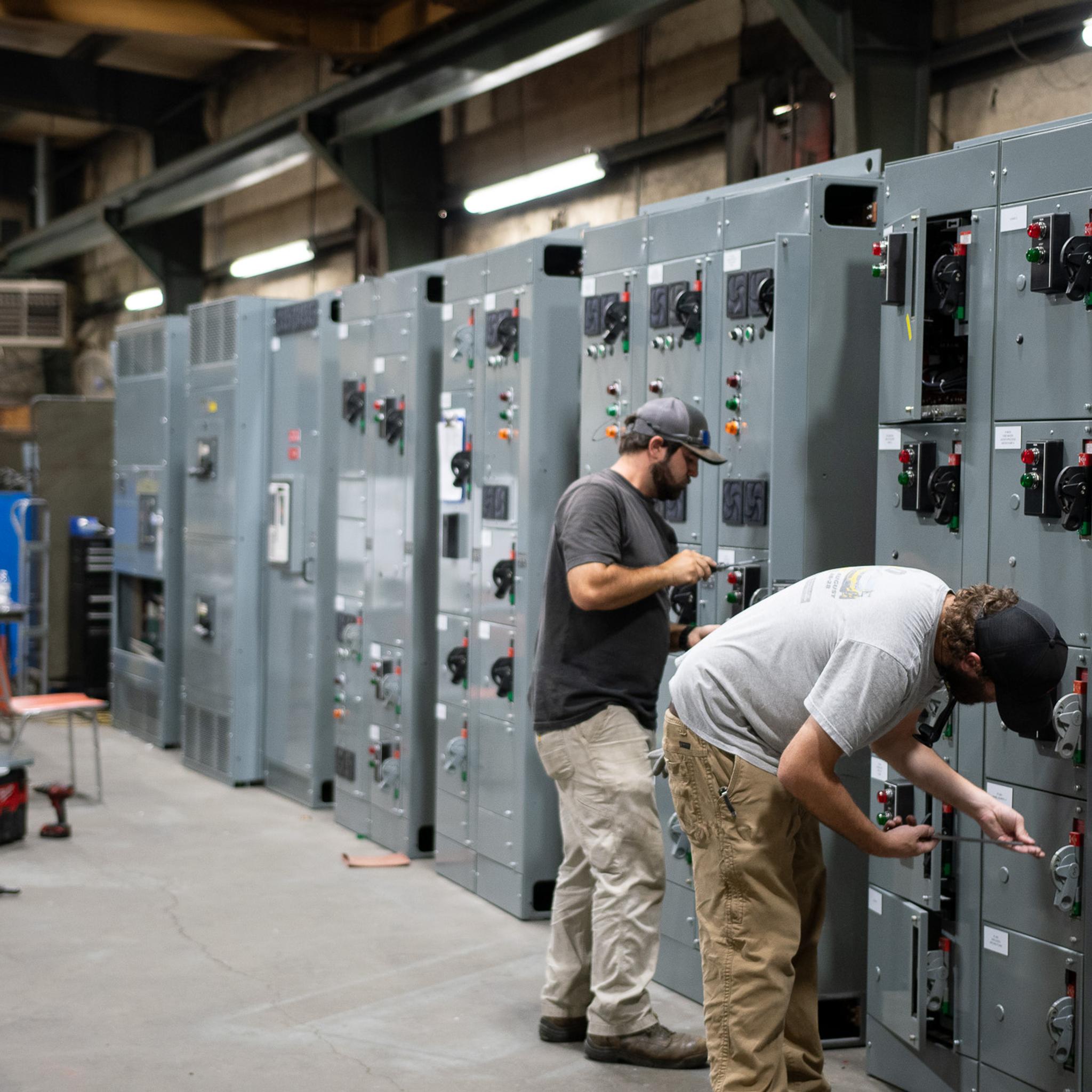 Technicians assemble and inspect industrial switchgear cabinets in an electrical service shop.