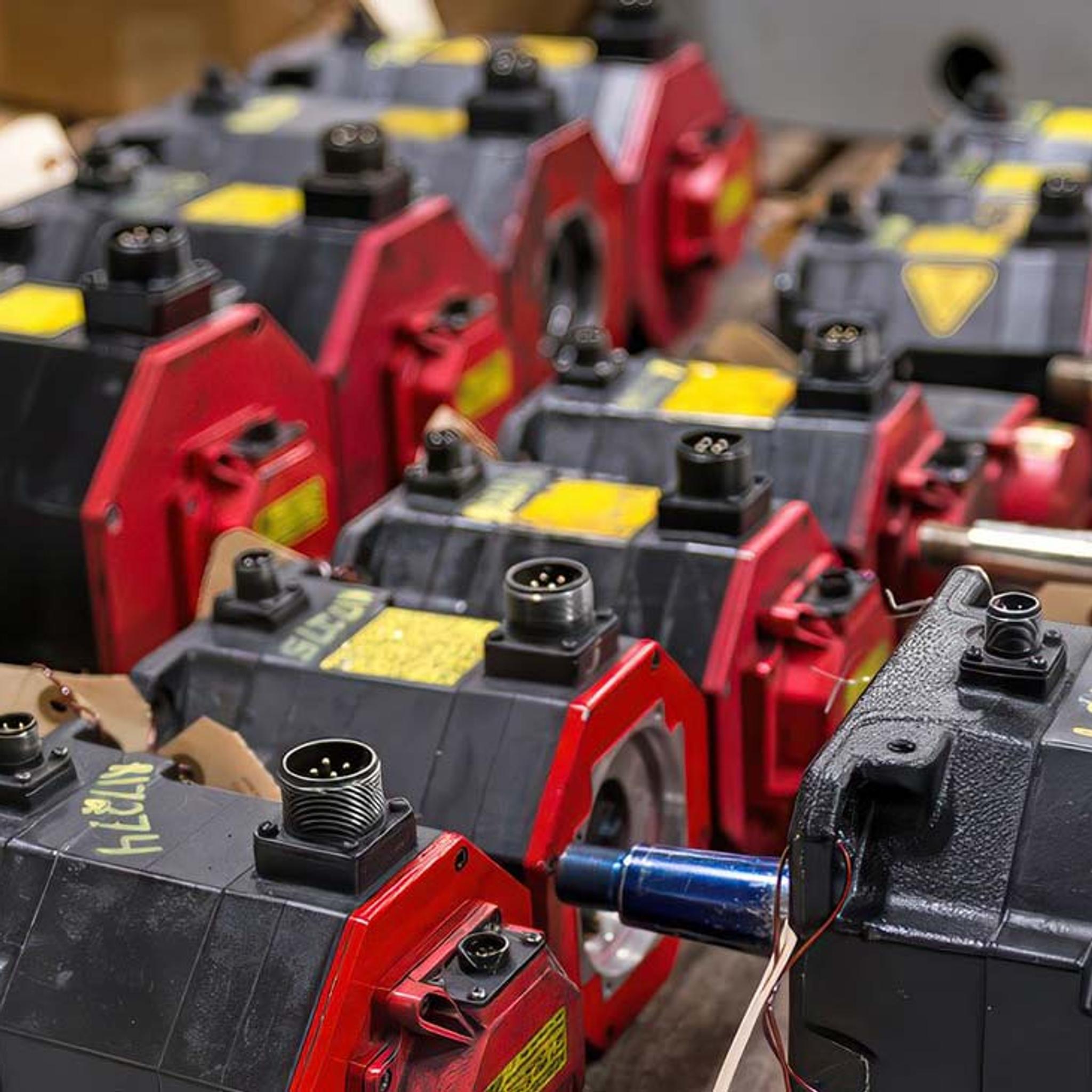 Rows of industrial servo motors with red mounting flanges and electrical connectors await service.