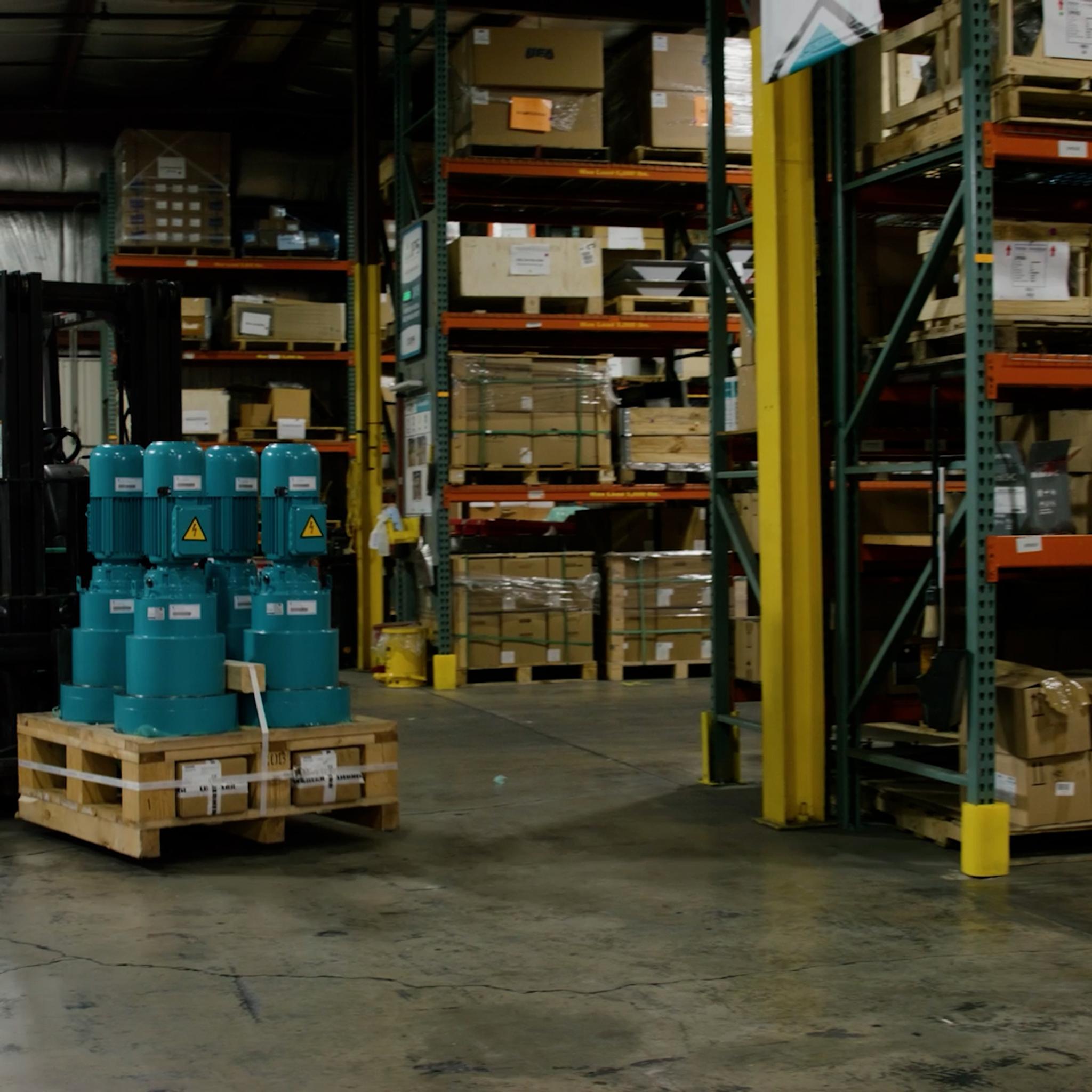 Forklift transports a pallet of industrial motors through a warehouse lined with equipment racks.