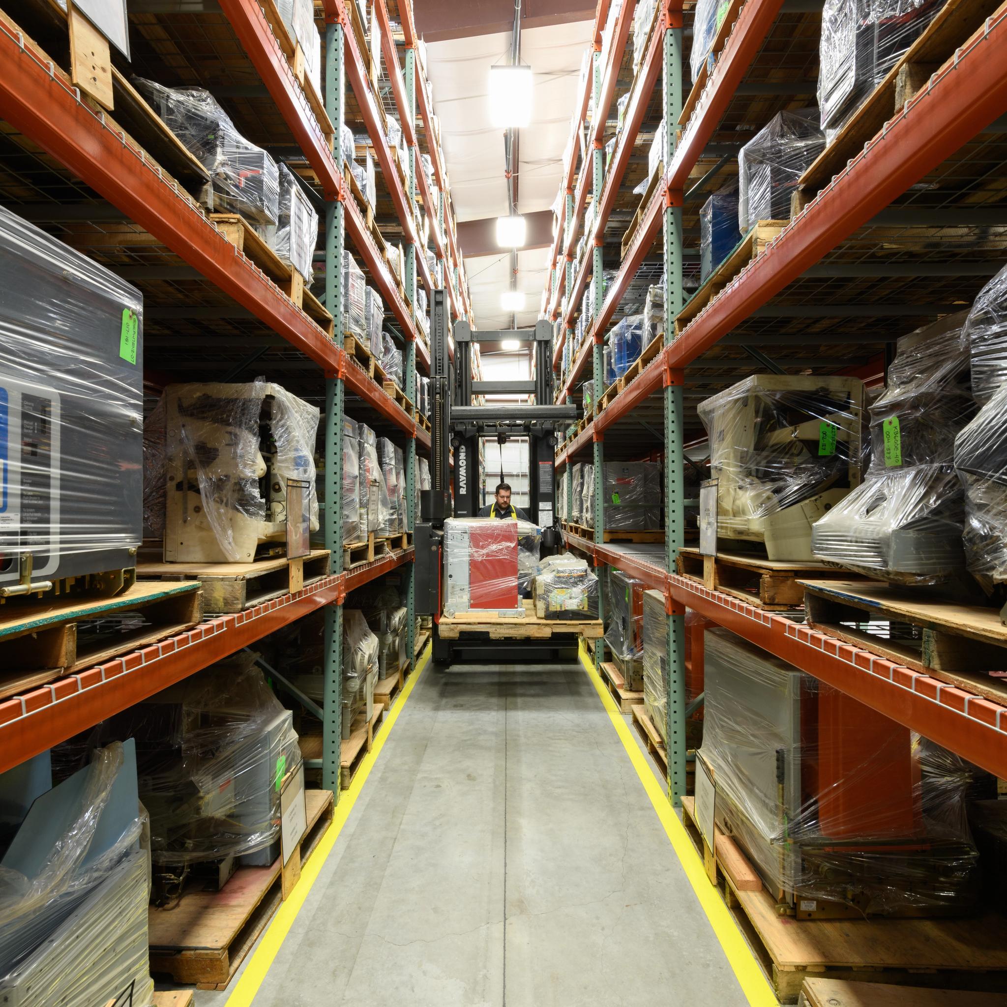 Forklift operator moves palletized electrical equipment through a warehouse aisle.