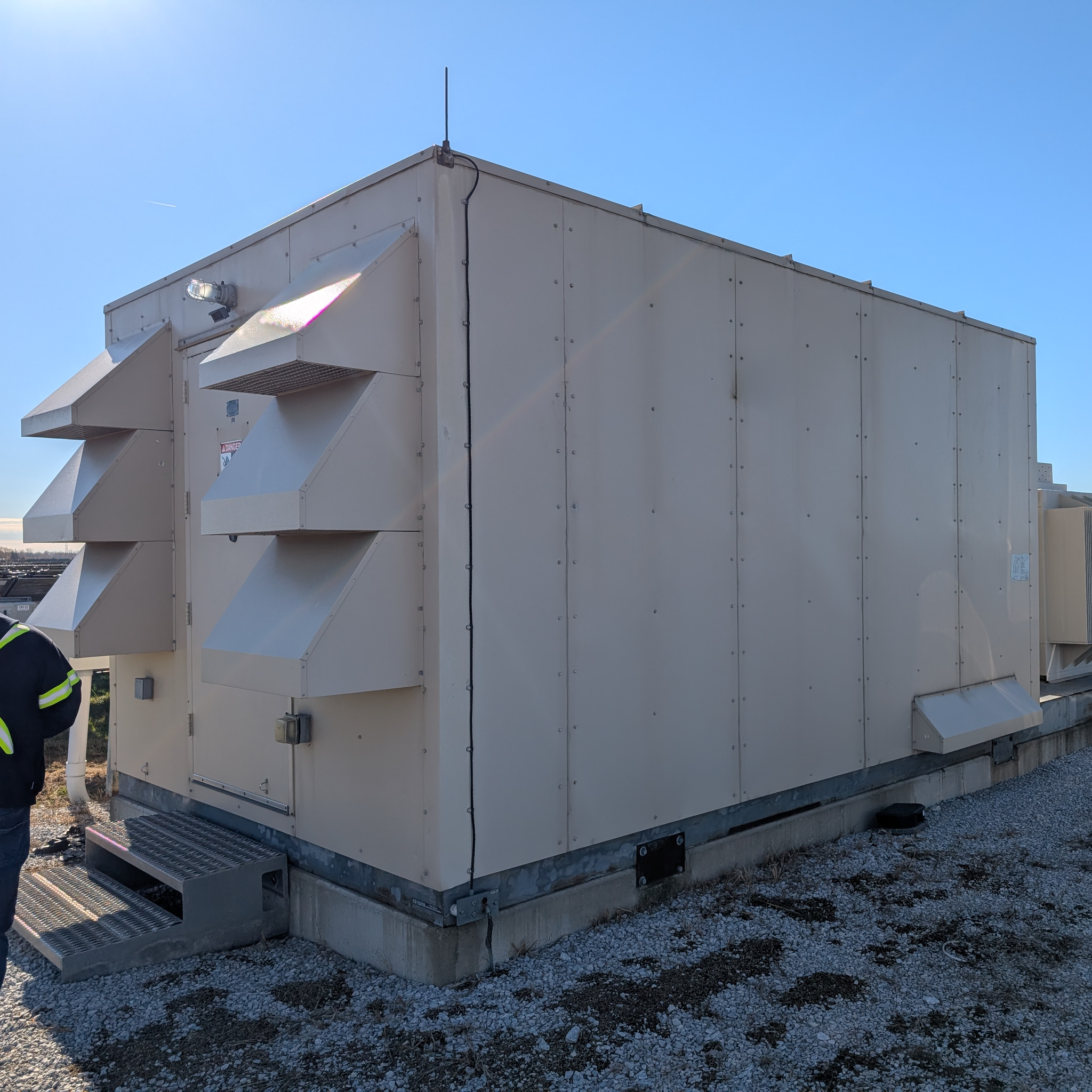Technician inspects a large outdoor electrical equipment enclosure with ventilation hoods.