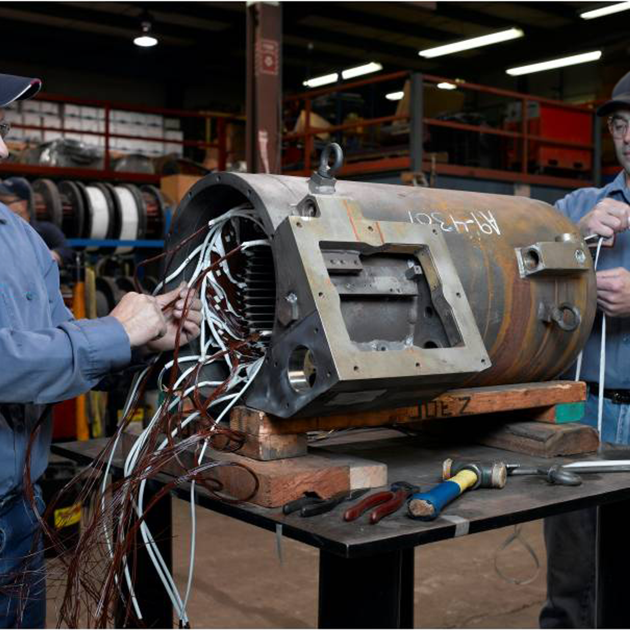 Two technicians repair and rewind a large industrial electric motor in a service workshop.