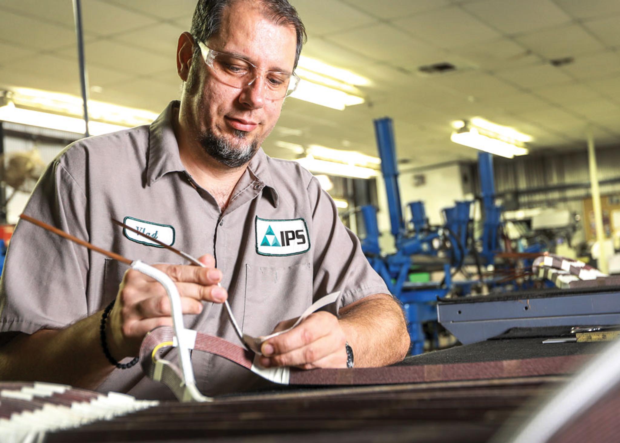 IPS technician wearing safety glasses repairs an electrical coil in a service workshop.