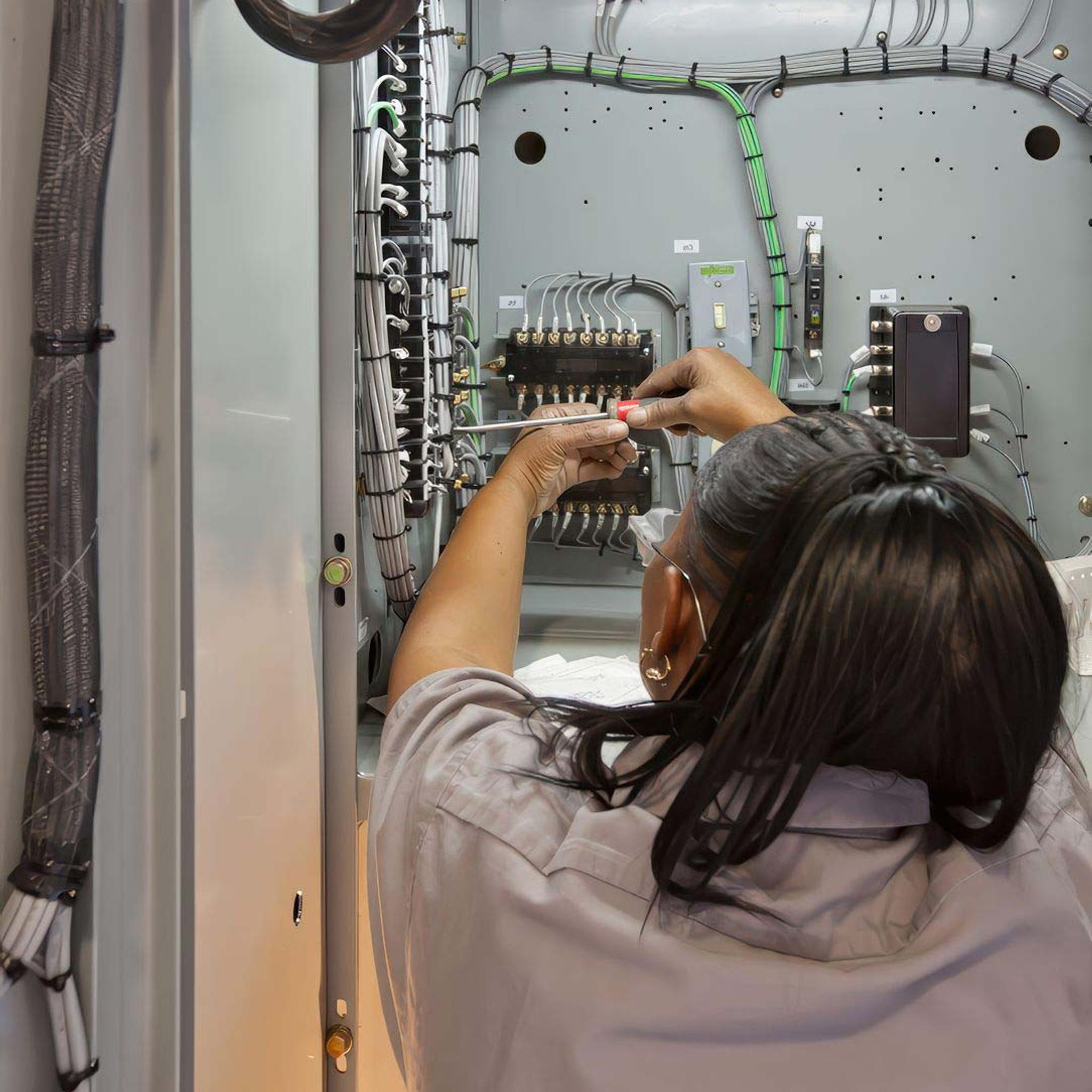 Technician uses a screwdriver to service wiring and terminal blocks inside an electrical control cabinet.