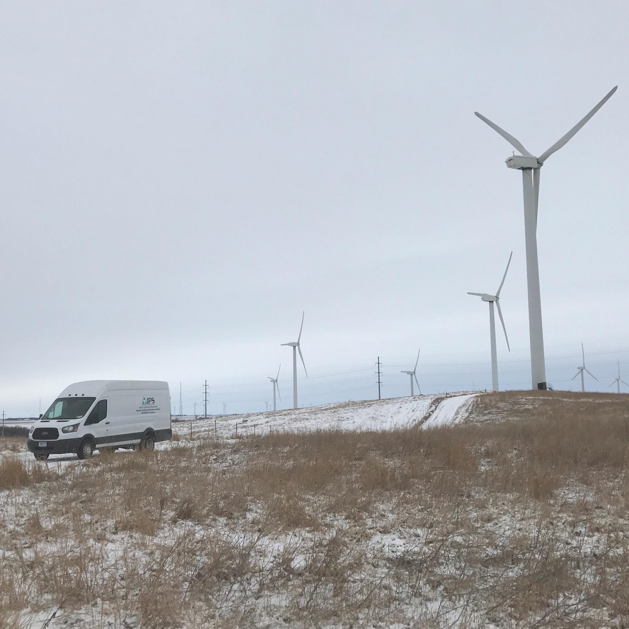 Camionnette de service IPS dans un parc éolien enneigé, entourée de plusieurs éoliennes.