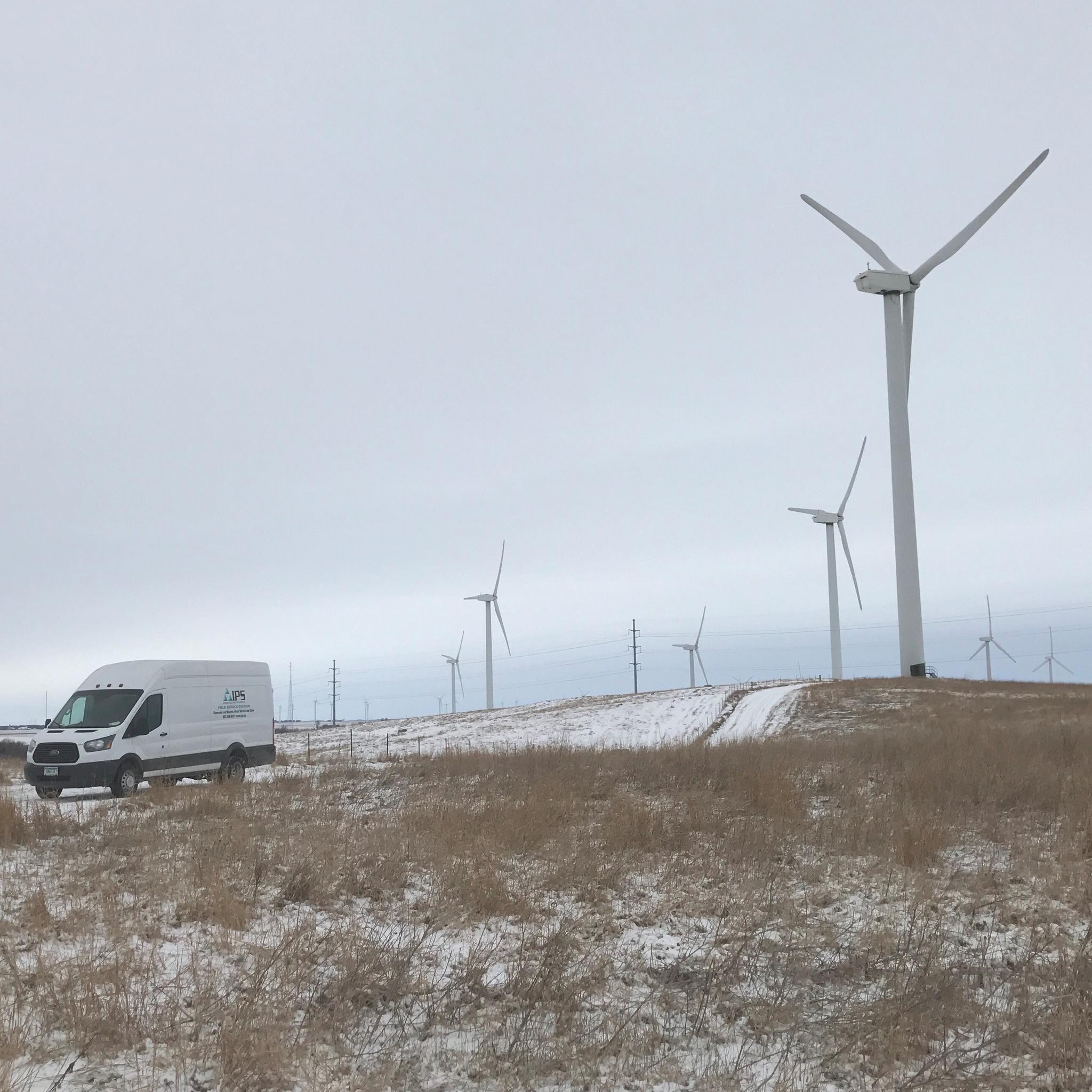 Camionnette de service IPS dans un parc éolien enneigé, entourée de plusieurs éoliennes.