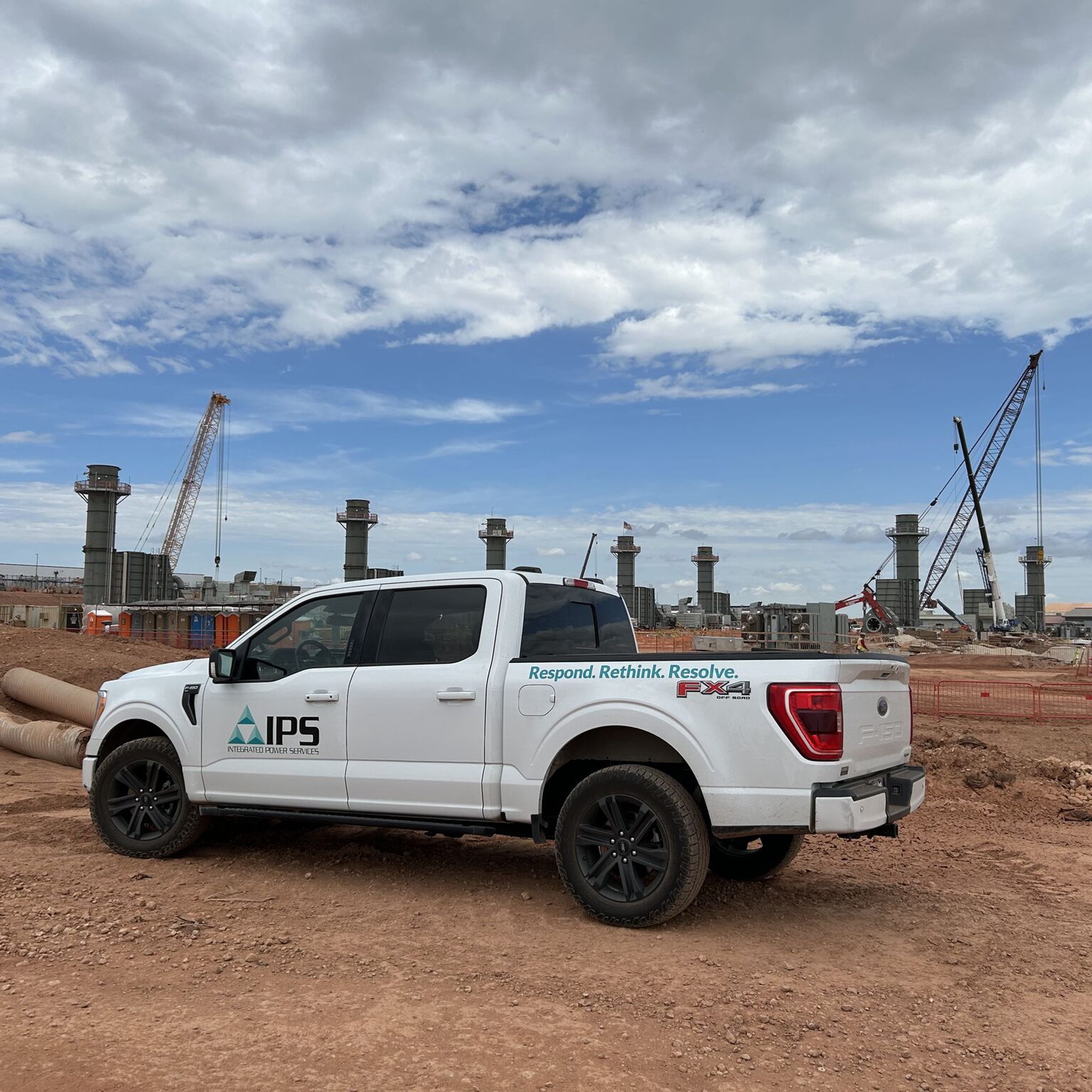 IPS service truck parked at an industrial construction site with cranes and power plant stacks.