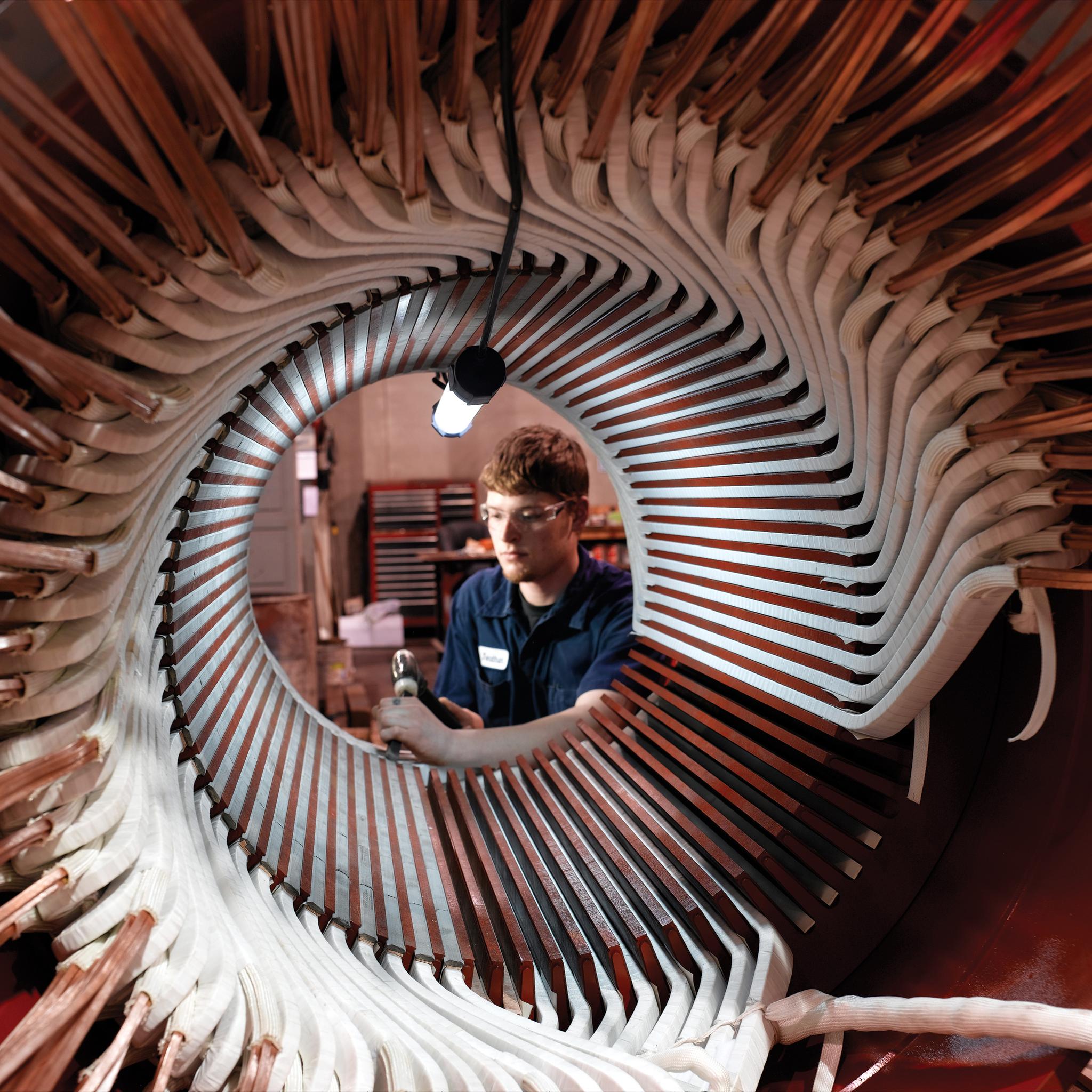 Technician repairs copper windings inside a large electric motor stator.