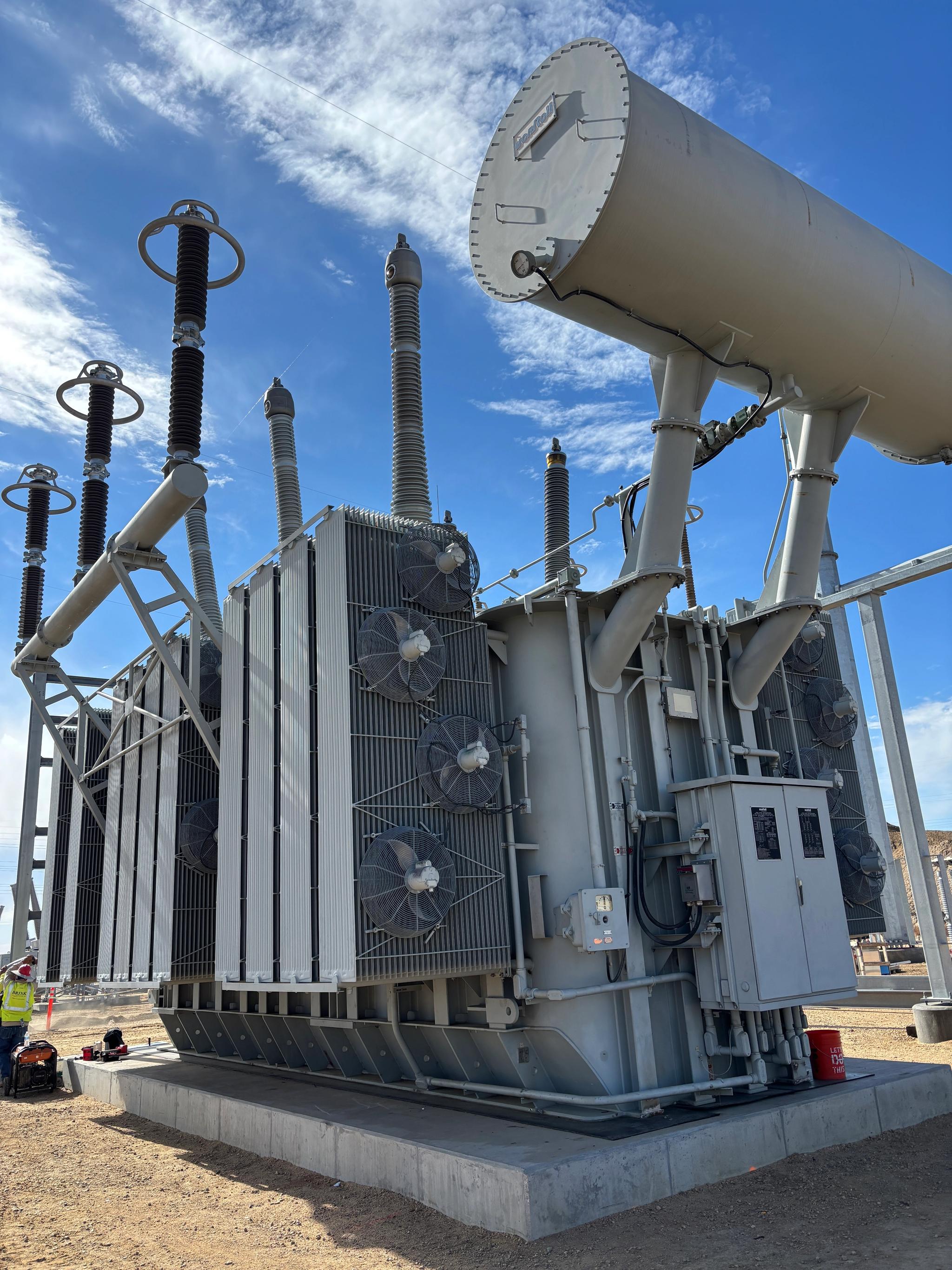 Large power transformer with cooling fans, bushings and conservator tank at an electrical substation.