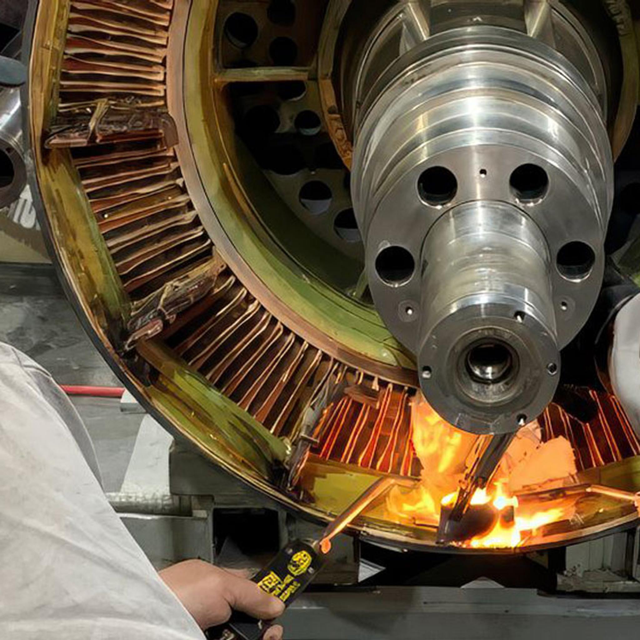 Technicians use torches to repair windings inside a large industrial motor.