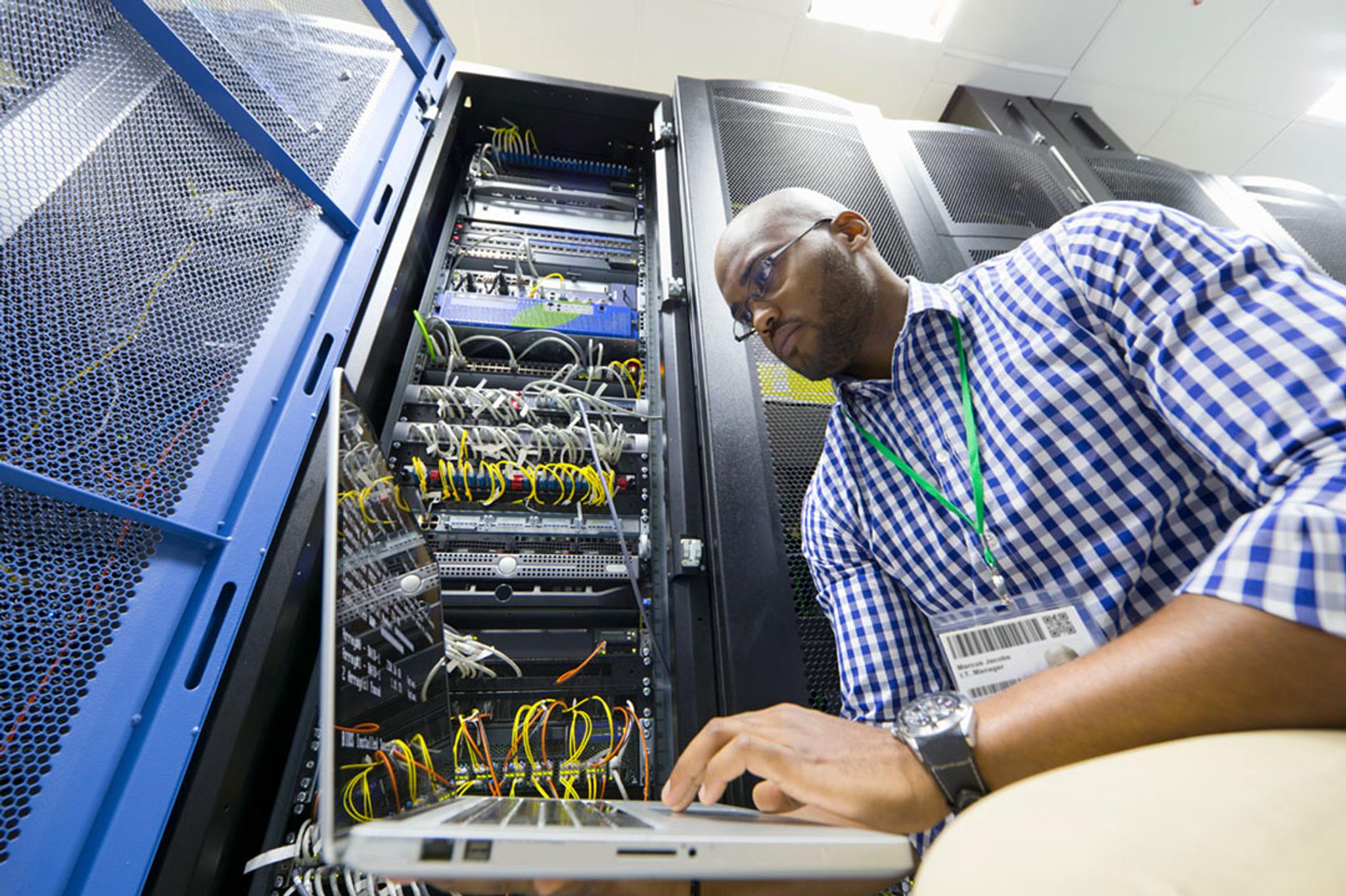 Técnico usa una computadora portátil para revisar servidores y cableado en un centro de datos.