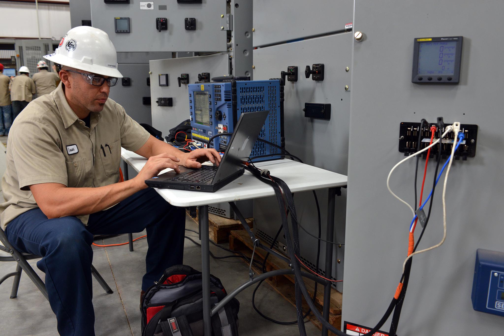 Technician uses a laptop and test equipment to service industrial switchgear.