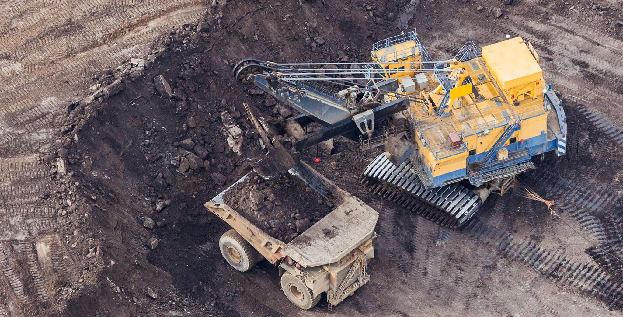 Excavadora eléctrica de minería carga roca en un camión volquete dentro de una mina a cielo abierto.