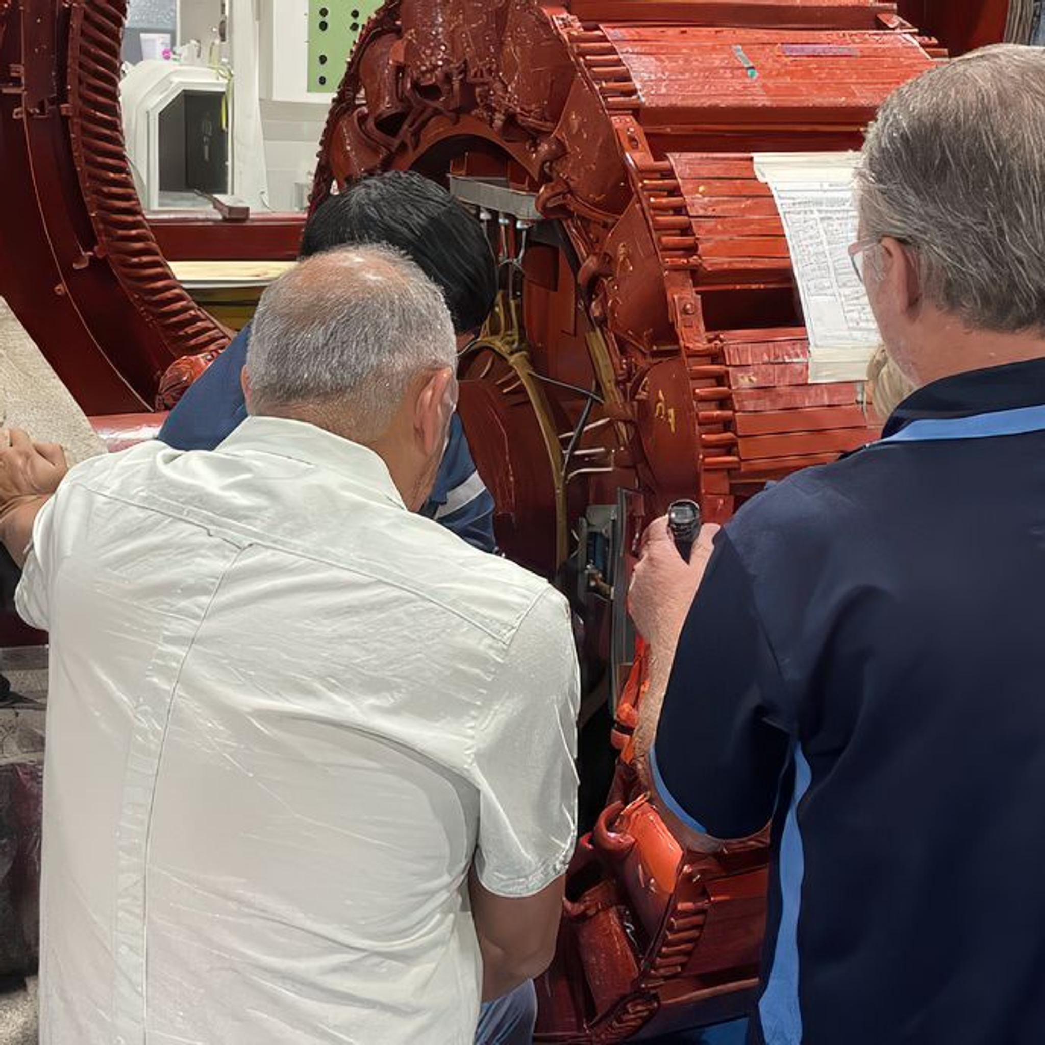 Technicians inspect and measure components inside a disassembled industrial electric motor.