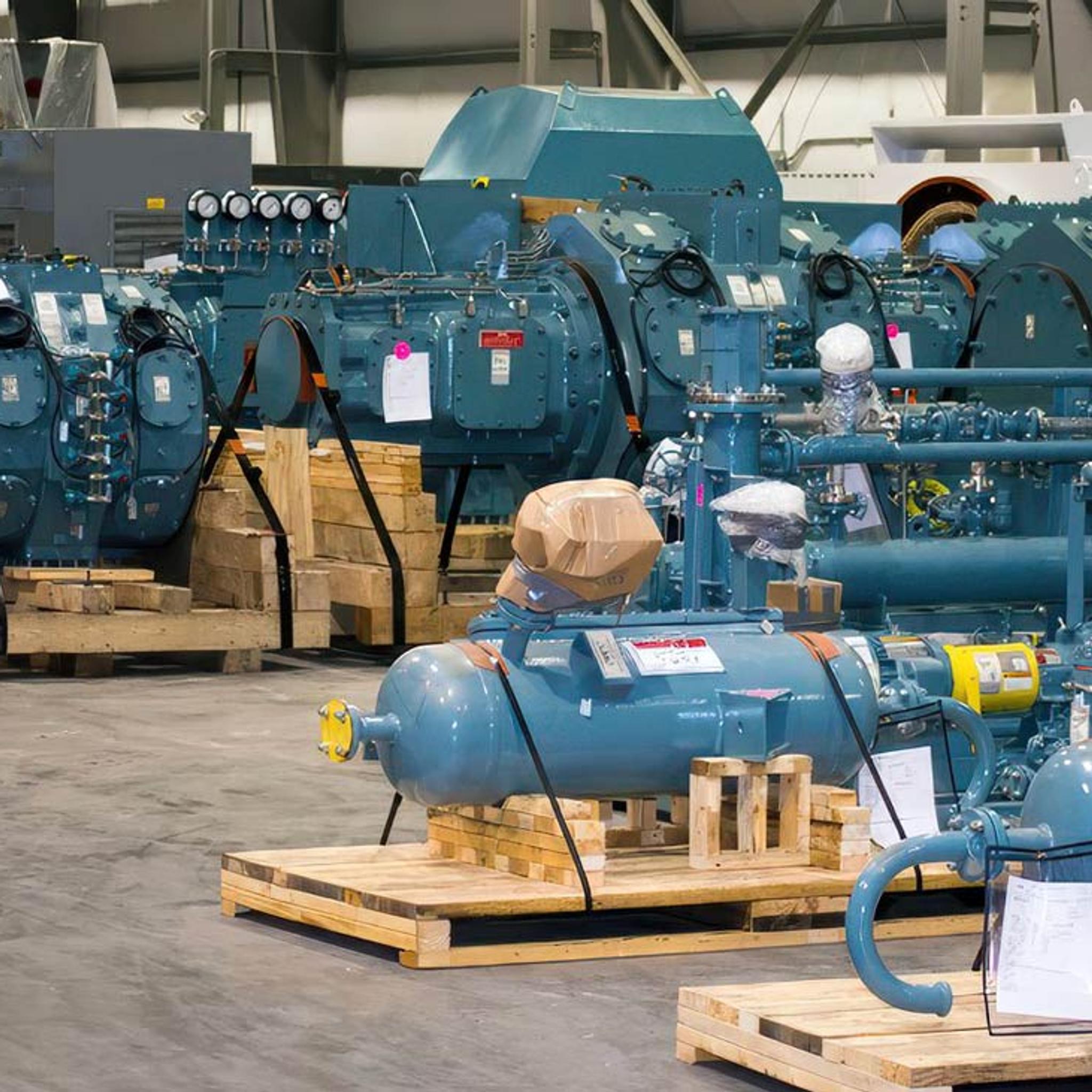 Industrial compressors and motors secured on wooden pallets inside an IPS service facility.
