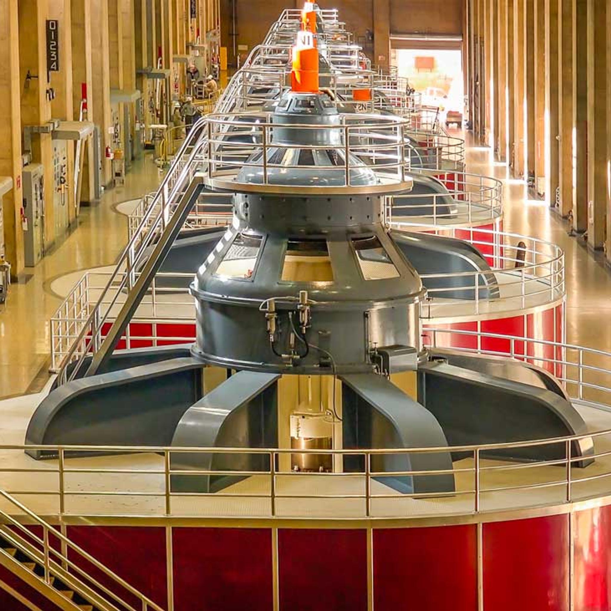 Row of hydroelectric generators with access platforms inside a power plant.