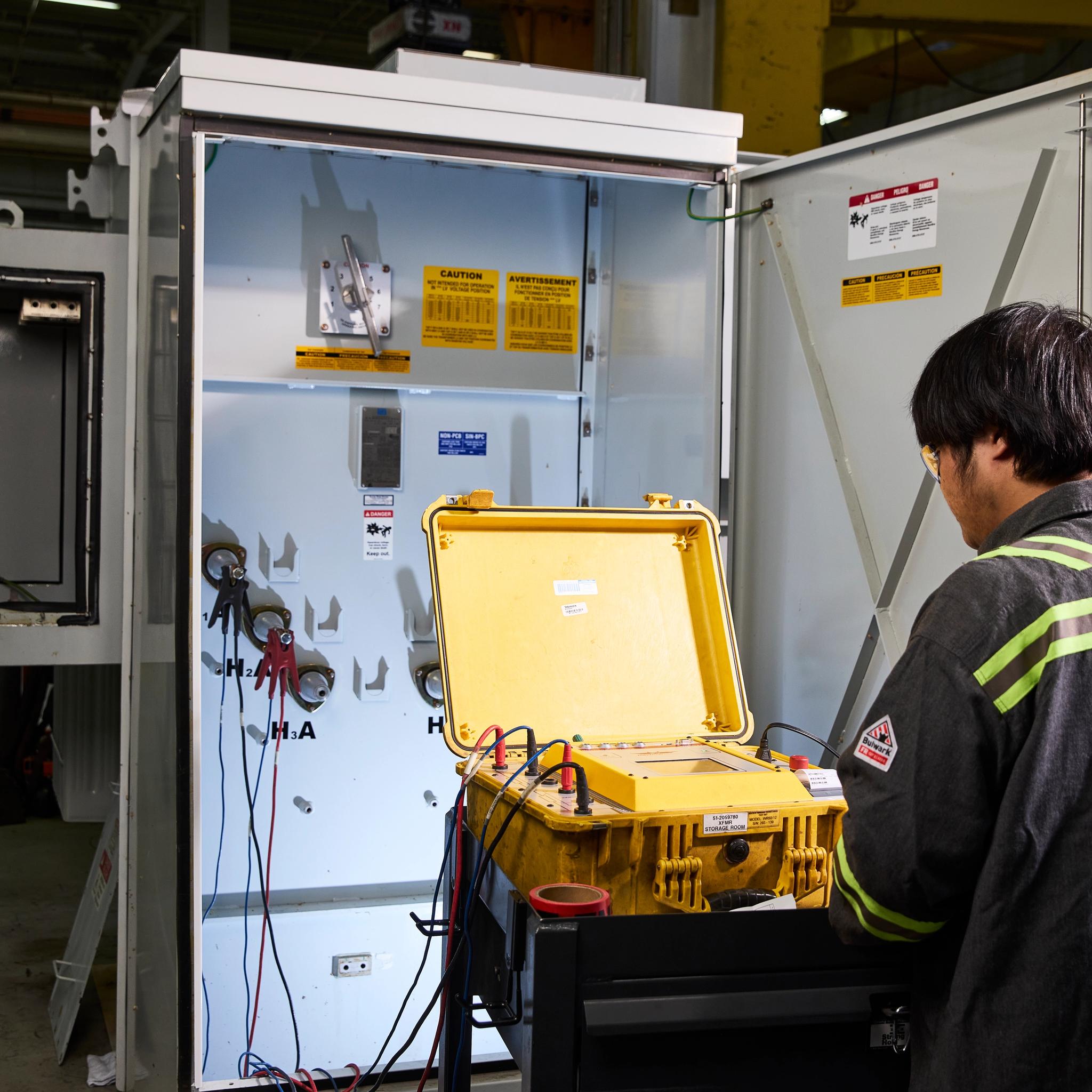 Technician uses electrical test equipment to inspect an open switchgear cabinet.