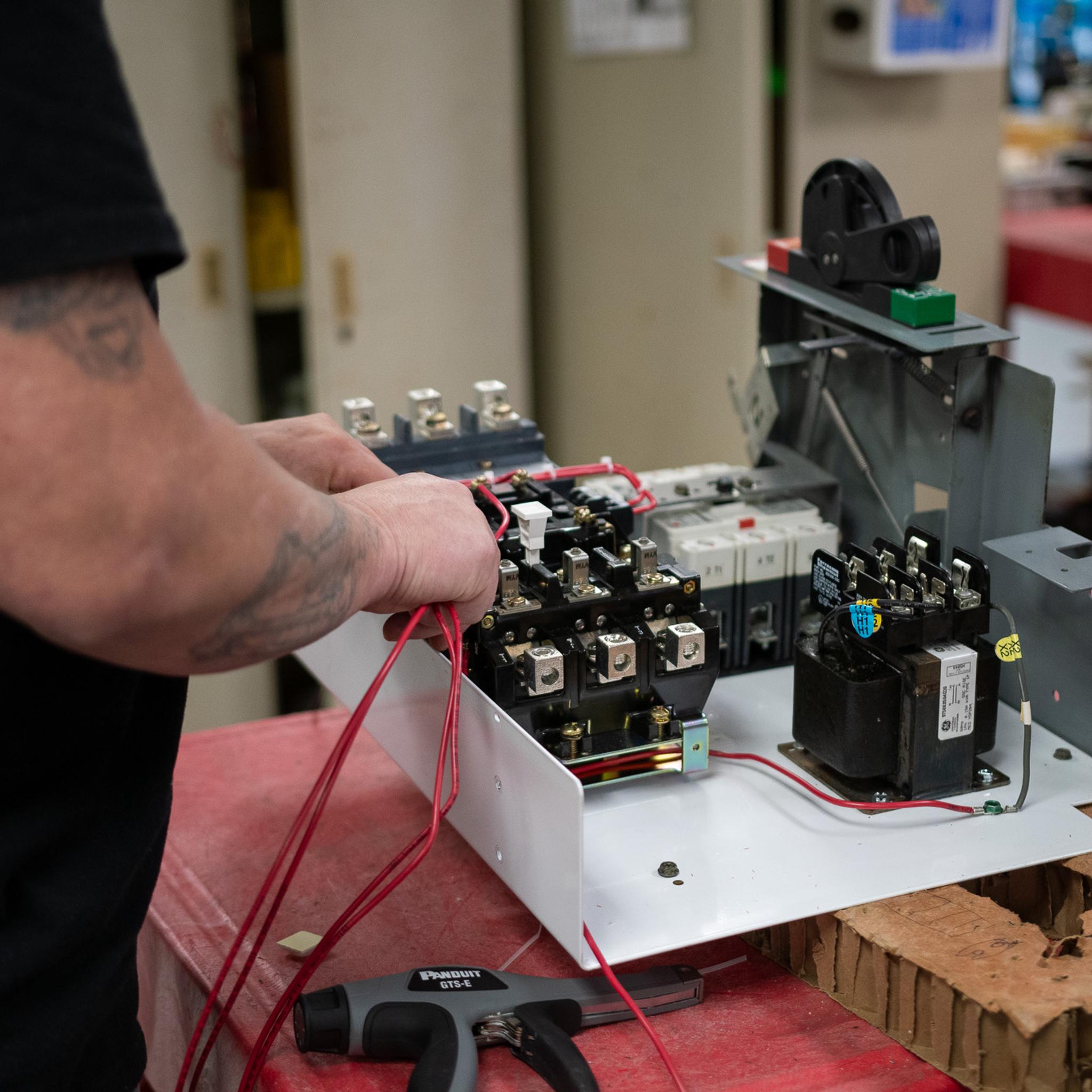 Technician connects test leads to electrical switchgear components on a workbench.