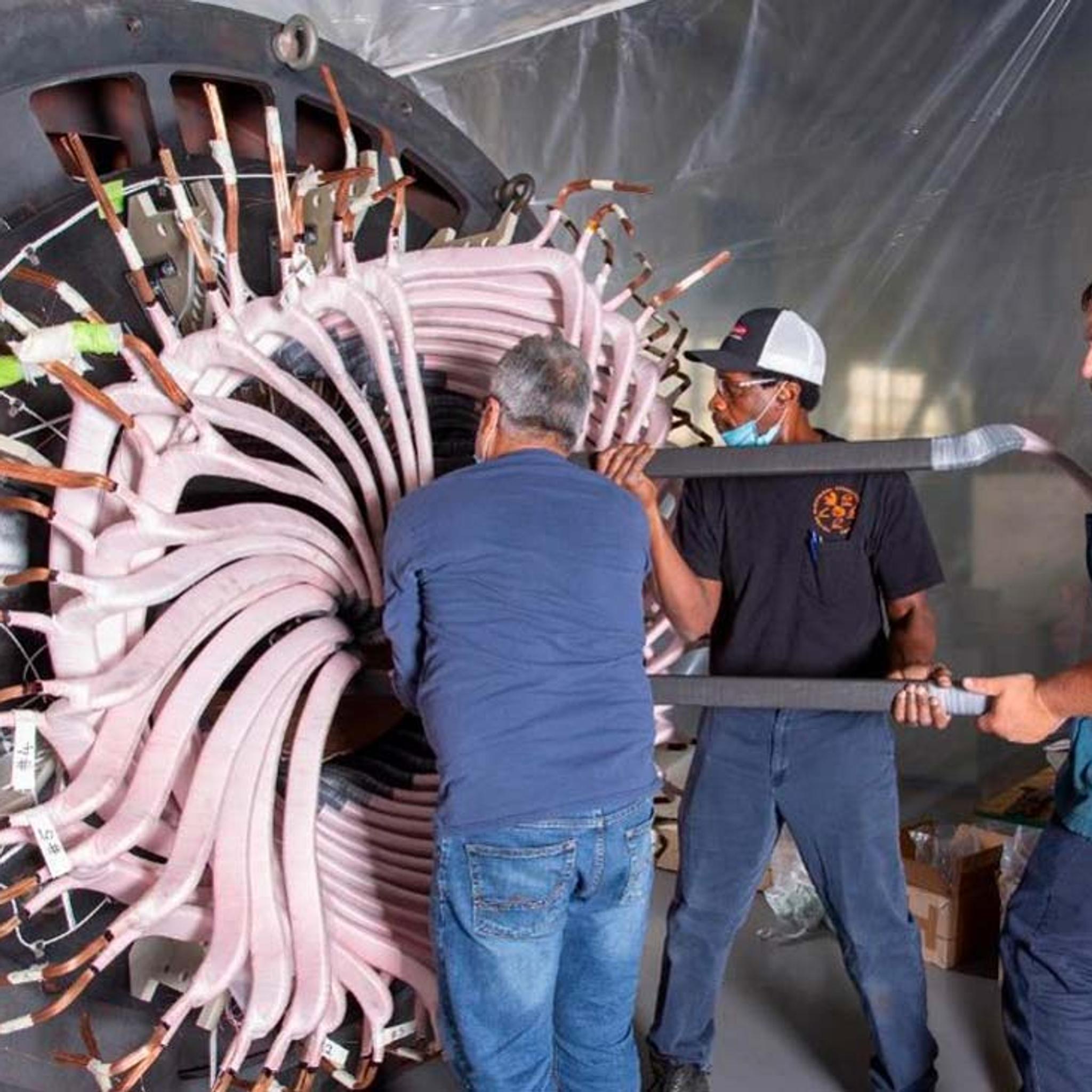 Technicians install insulated stator windings in a large industrial electric motor.