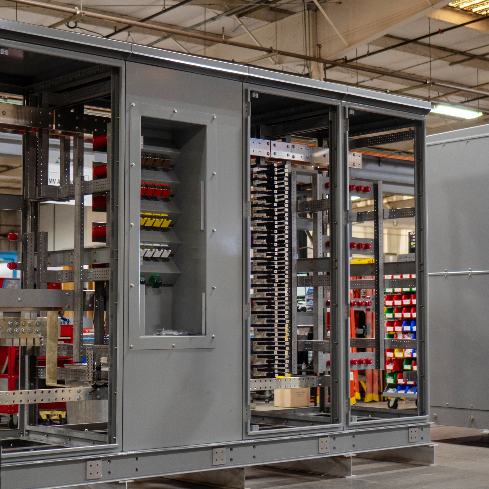 Open industrial switchgear cabinets with busbars and electrical components on a factory floor.