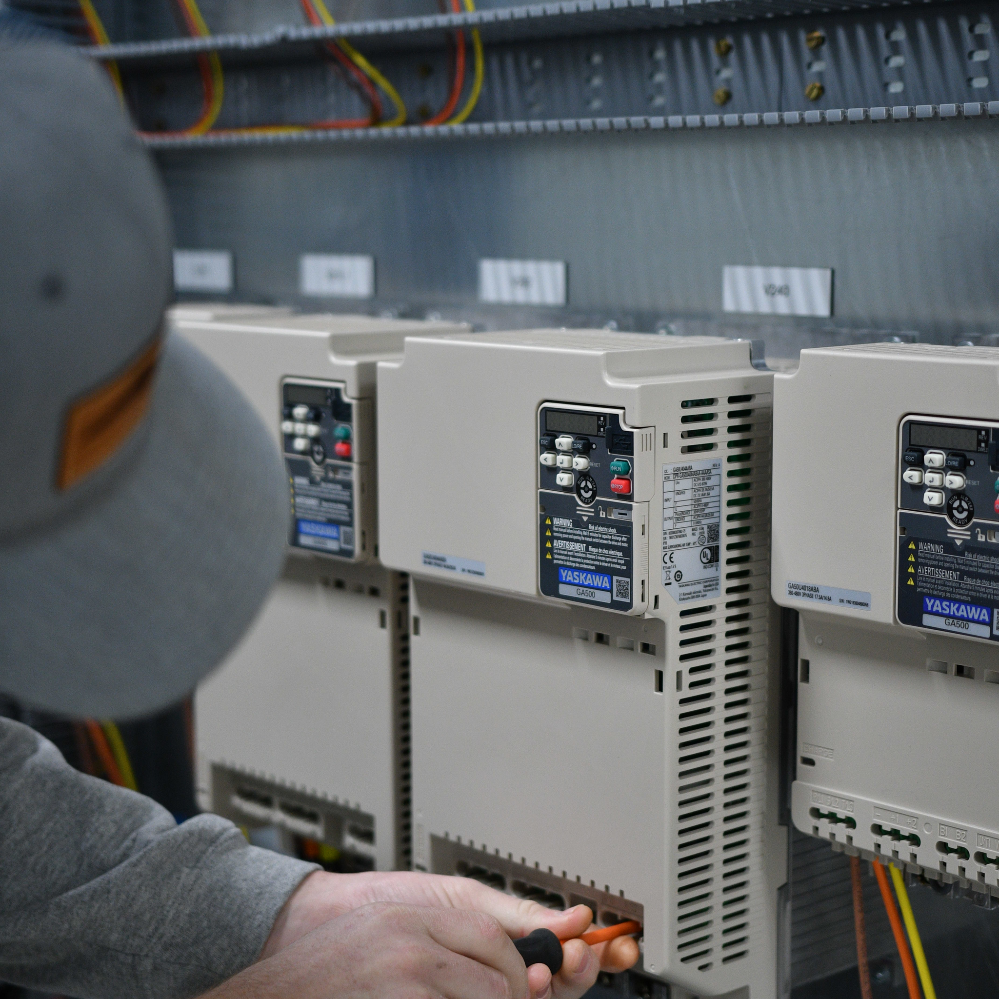 Technician uses a screwdriver to service Yaskawa variable frequency drives in an electrical control panel.
