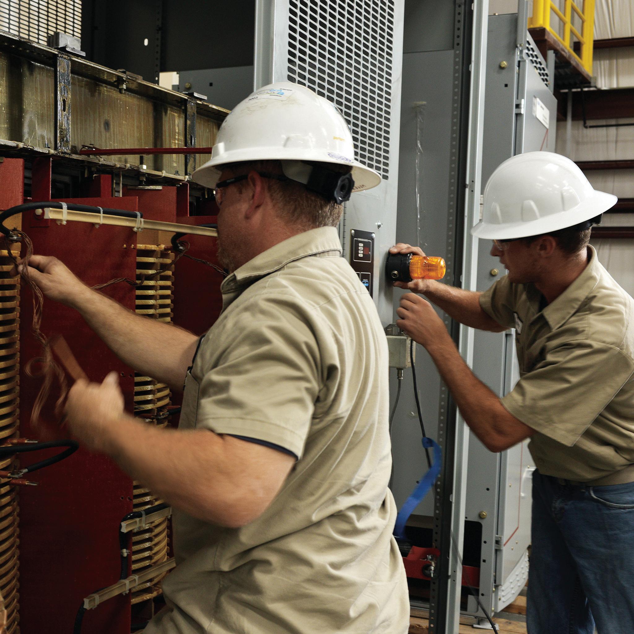 Technicians inspect transformer windings and electrical connections inside industrial switchgear.